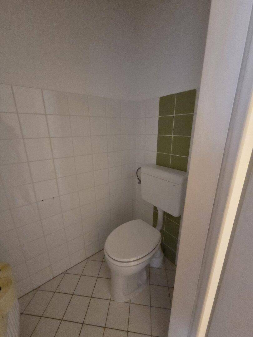 Kleines WC mit weiß-grünen Fliesen und einer Toilette, praktisch und funktional gestaltet.