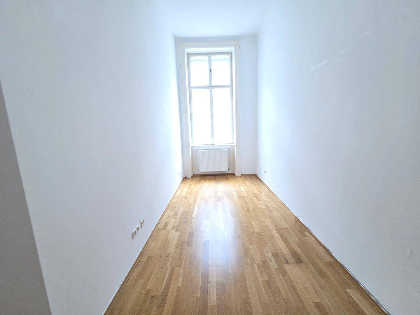 Langer, heller Raum mit Parkettboden und Fenster am Ende, ideal als Flur oder Ankleidezimmer nutzbar.