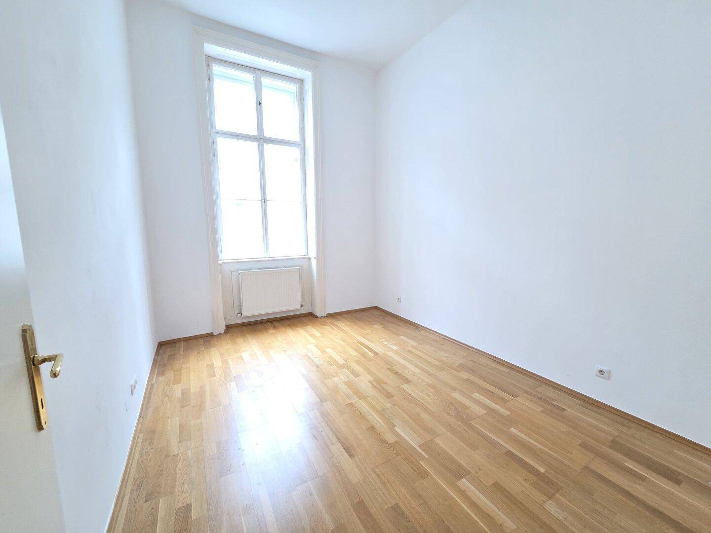 Gemütliches Zimmer mit Parkettboden und einem großen Fenster, gut geeignet als Schlafzimmer oder Büro.