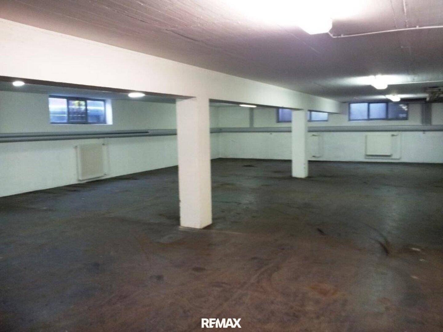 Großer, offener Kellerraum mit tragenden Säulen und kleinen Fenstern nahe der Decke.