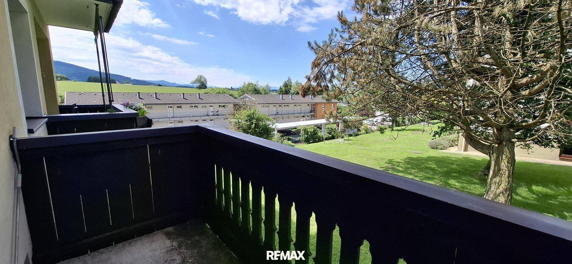 Balkon mit traditionellem Holzgeländer bietet einen weiten Blick über die grüne Landschaft und Nachbargebäude.