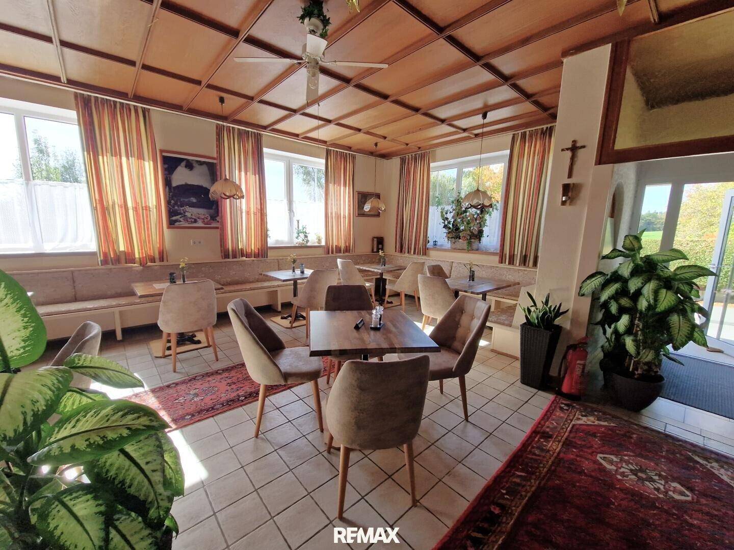 Heller Speisesaal mit Holzkassettendecke, Fliesenboden und Blick auf den Außenbereich durch die Tür.