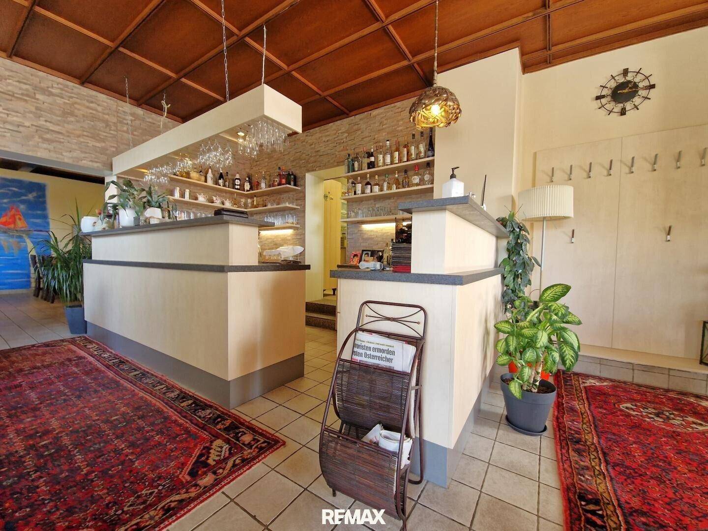 Gut ausgestatteter Barbereich mit Theke, Regalen voller Flaschen und Holzkassettendecke.