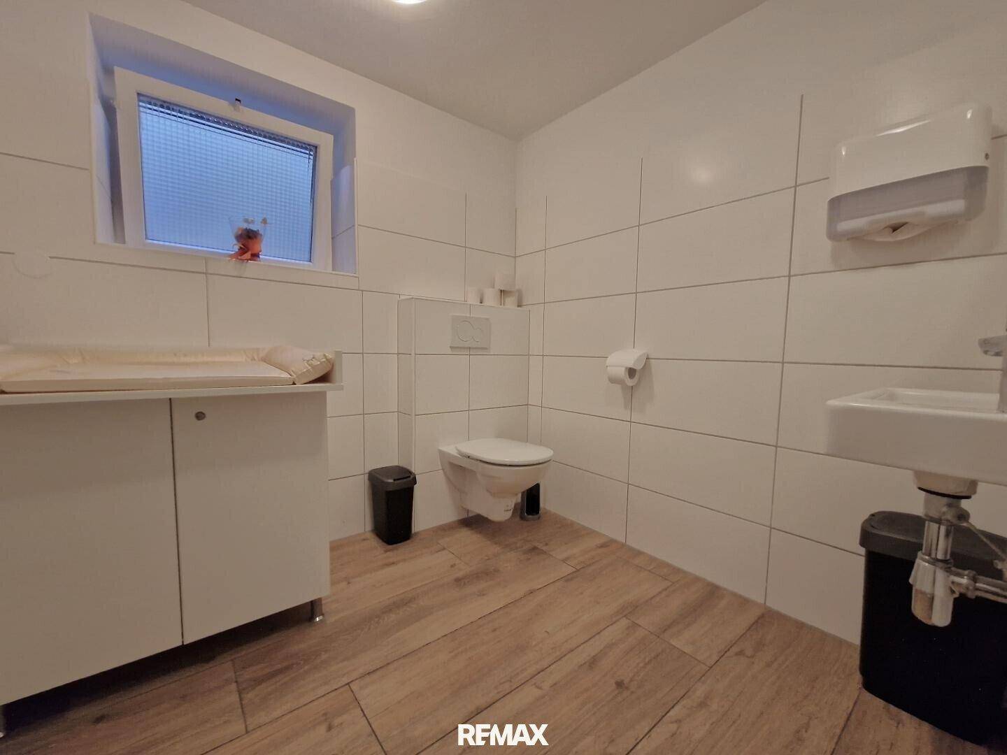 Familienfreundlicher Waschraum mit Toilette, Wickeltisch, Waschbecken und einem Fenster für Tageslicht.