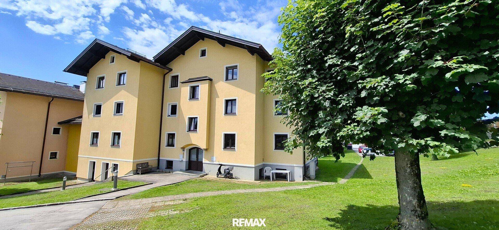 Gelbes Mehrfamilienhaus mit traditioneller Architektur und grüner Umgebung unter blauem Himmel.