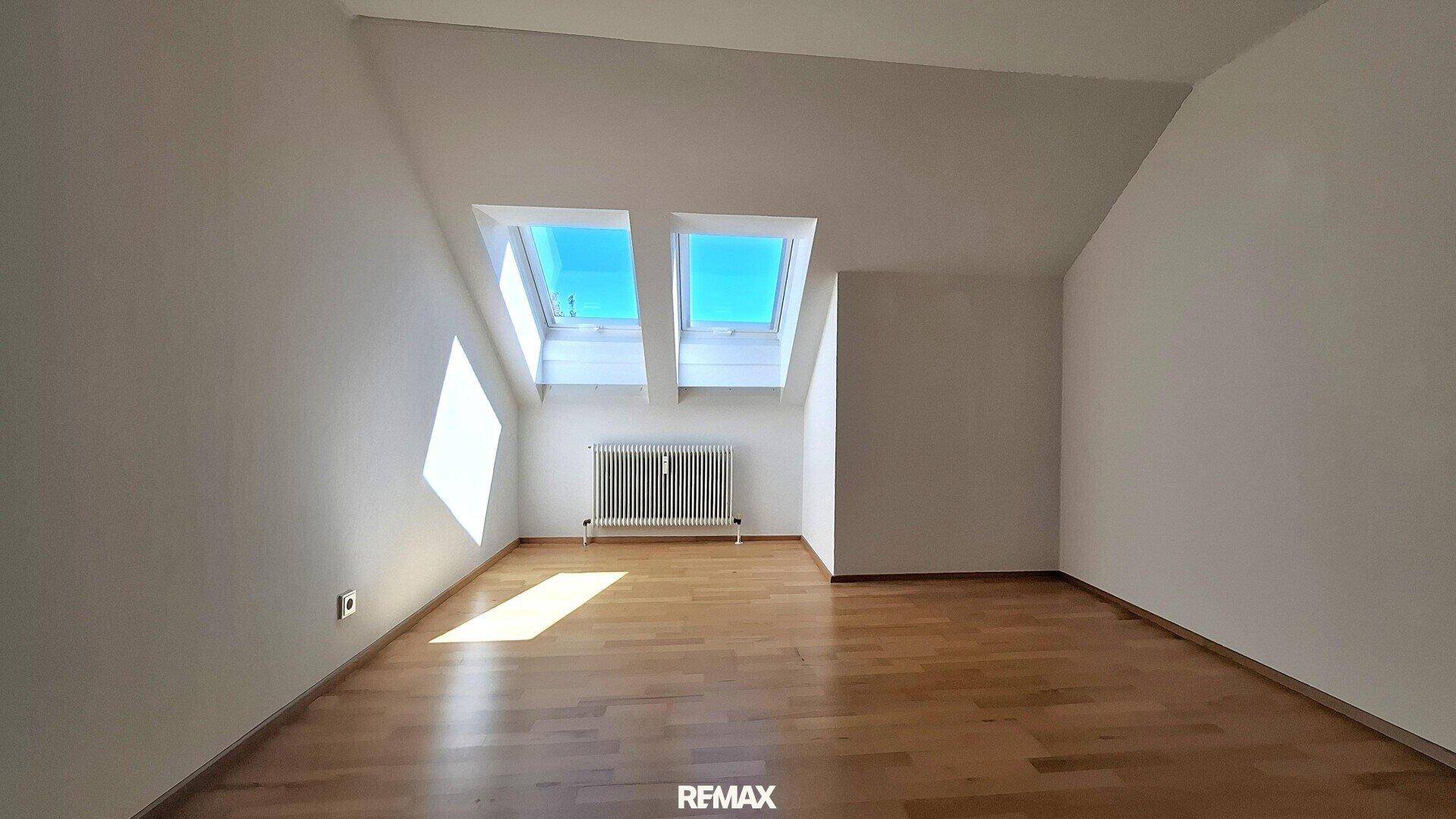 Geräumiger Dachgeschossraum mit Parkettboden, Dachfenstern und hellem Tageslicht.