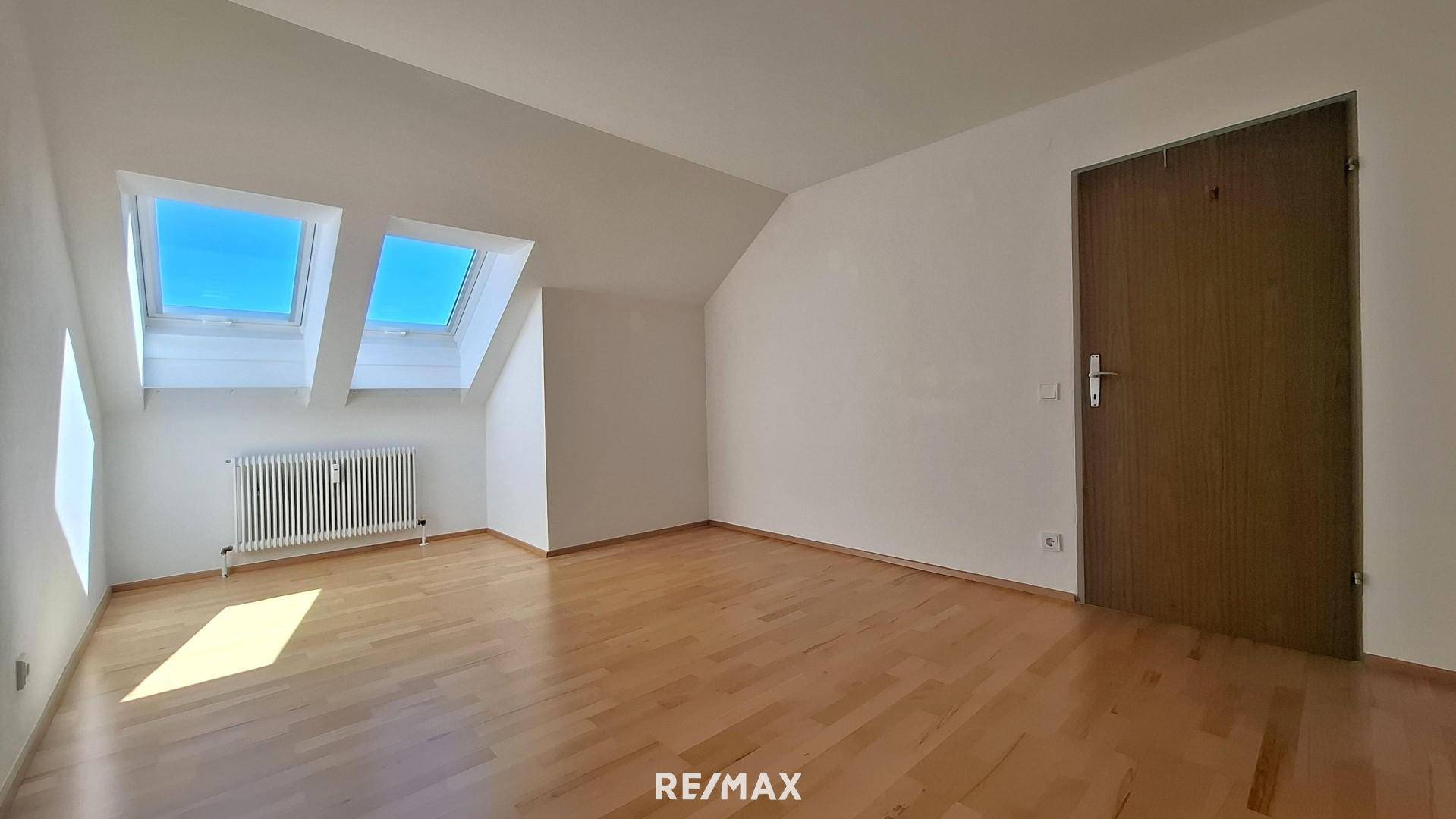 Helles Dachzimmer mit Parkettboden, weiß gestrichenen Wänden und einer Holztür, die den Raum abschließt.