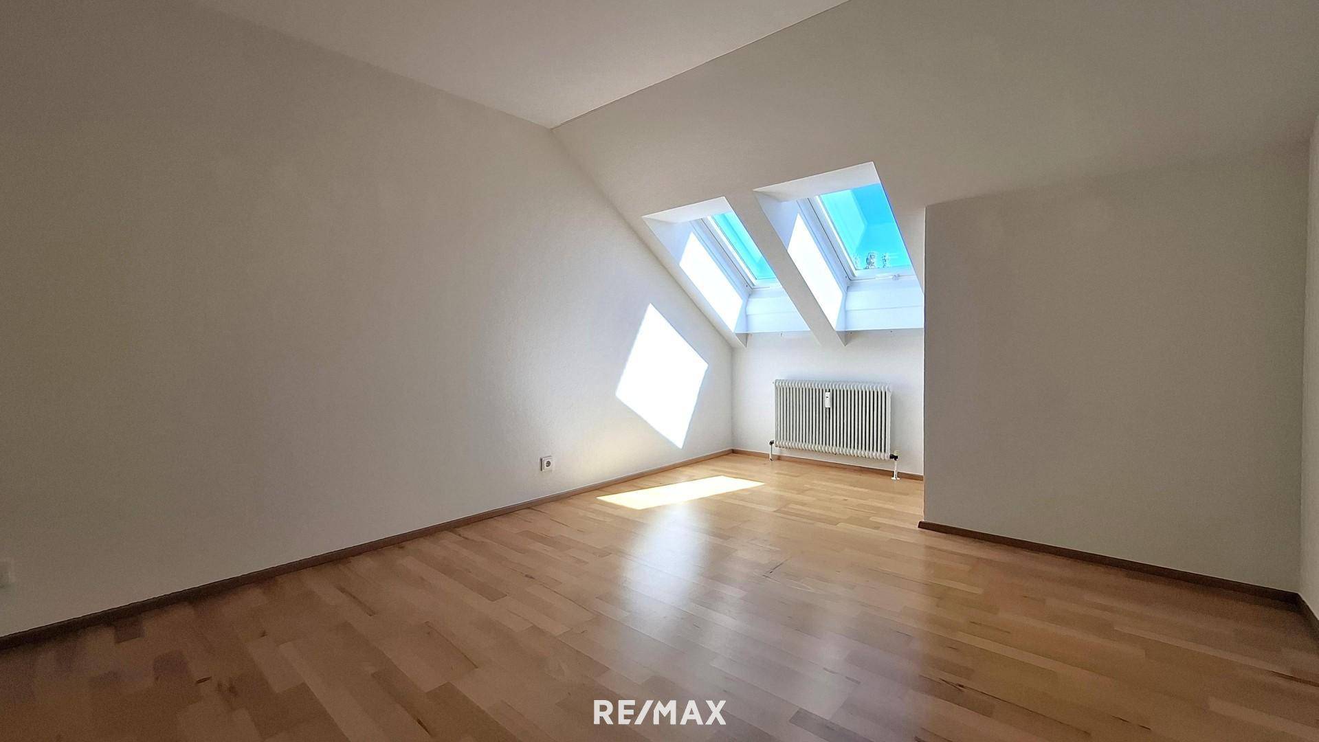 Geräumiges Dachzimmer mit Parkettboden, schrägen Wänden und hellen Dachfenstern, die den Raum erhellen.