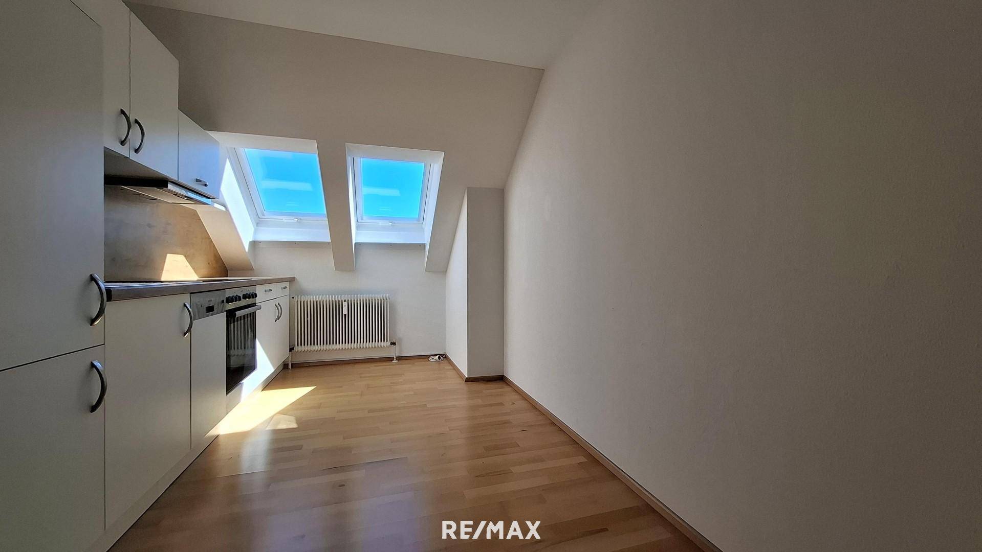 Moderne Küchenzeile mit weißen Fronten und integriertem Backofen in einem lichtdurchfluteten Dachzimmer.