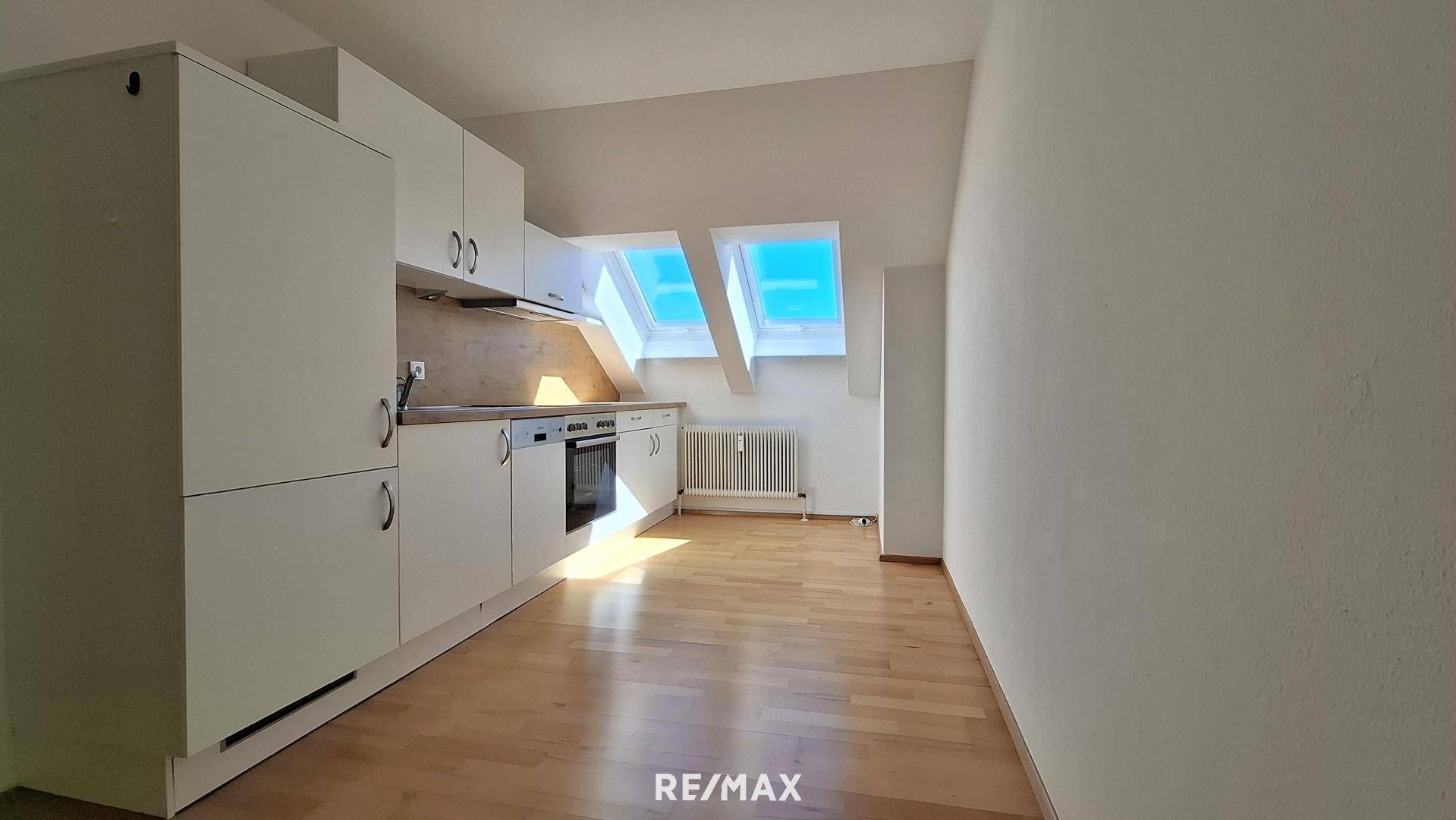 Funktionale Küchenzeile in einem hellen Dachzimmer mit weißen Schränken, Backofen und Parkettboden.