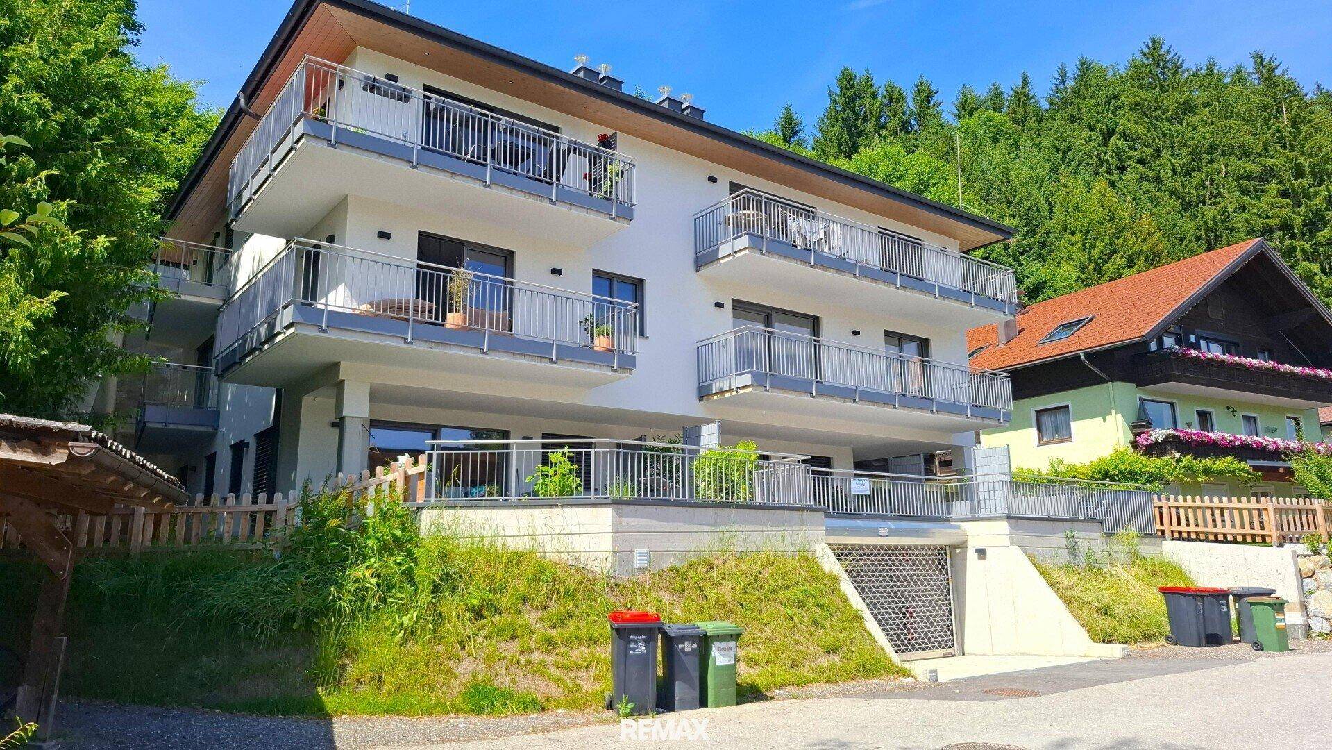 Modernes Mehrfamilienhaus mit mehreren Balkonen, umgeben von grüner Natur und Bergblick.