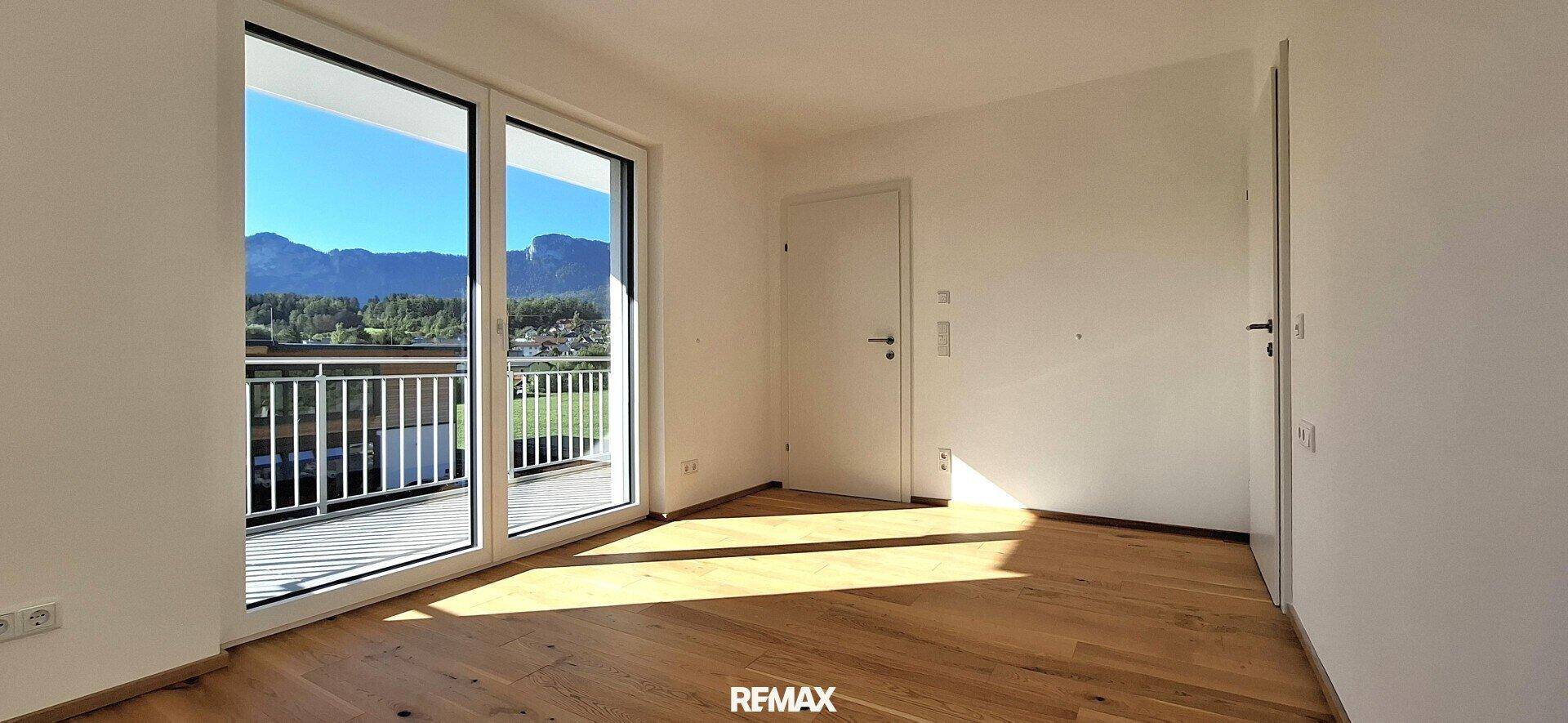 Geräumiger Raum mit Holzboden, großen Fenstern und direktem Zugang zum Balkon mit Bergblick.