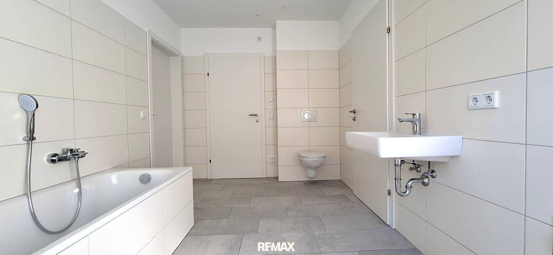 Helles Badezimmer mit Badewanne, Dusche, WC und modernem Waschbecken, komplett gefliest.