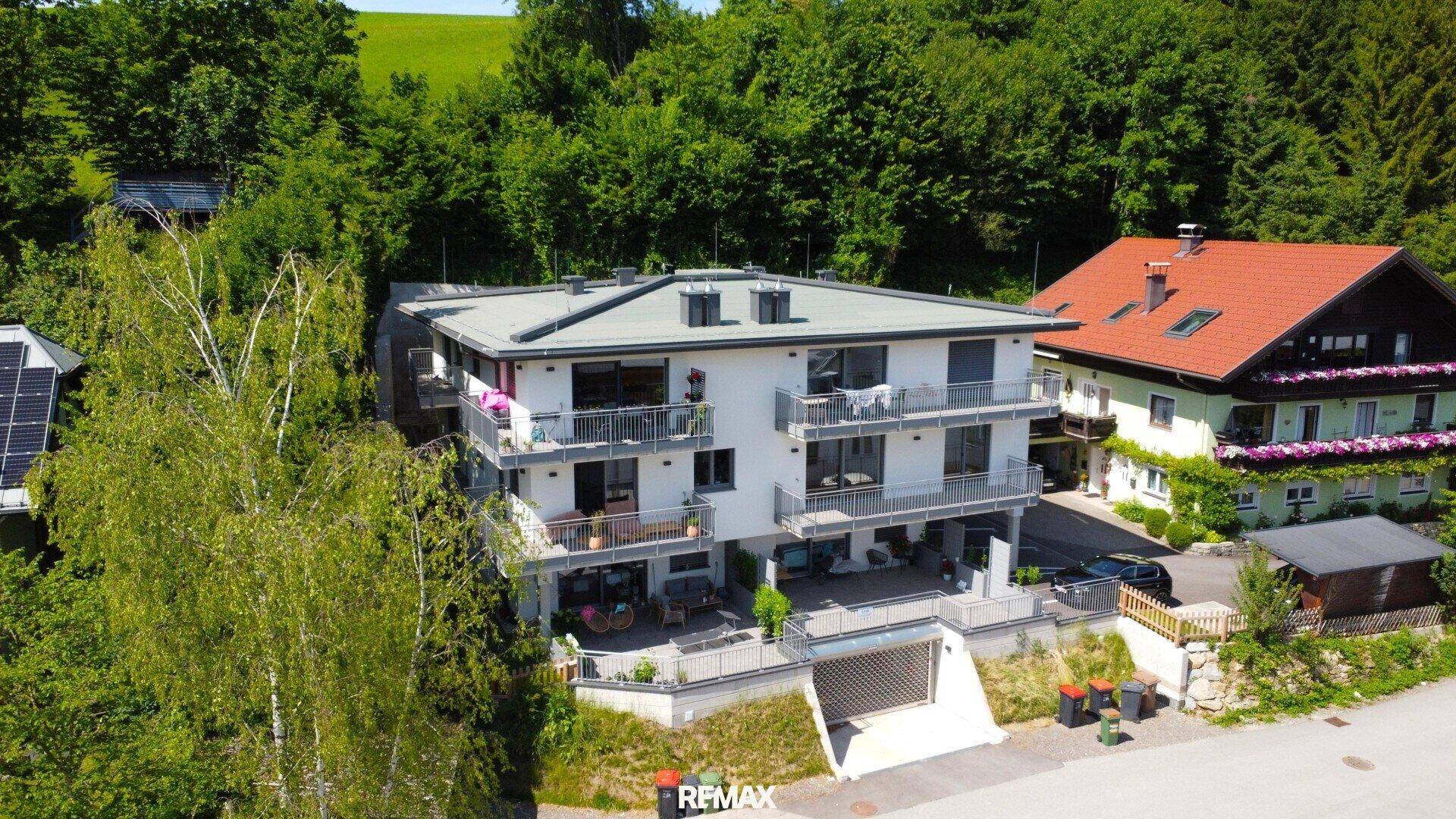 Luftaufnahme des modernen Wohngebäudes mit Flachdach, umgeben von Bäumen und Bergblick.
