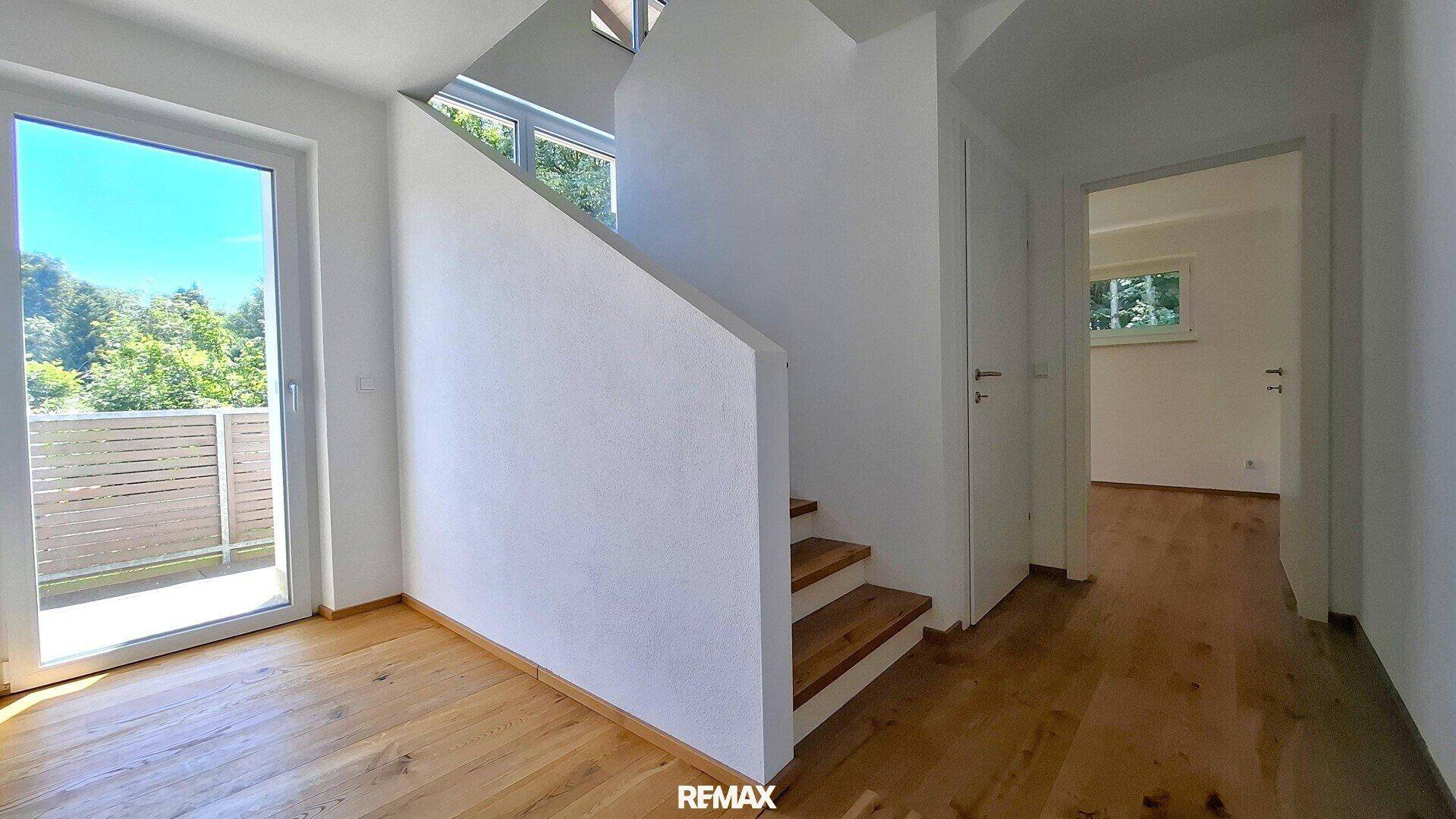 Heller Flur mit Holztreppe, Holzboden und Zugang zu einem Balkon oder einer Terrasse.