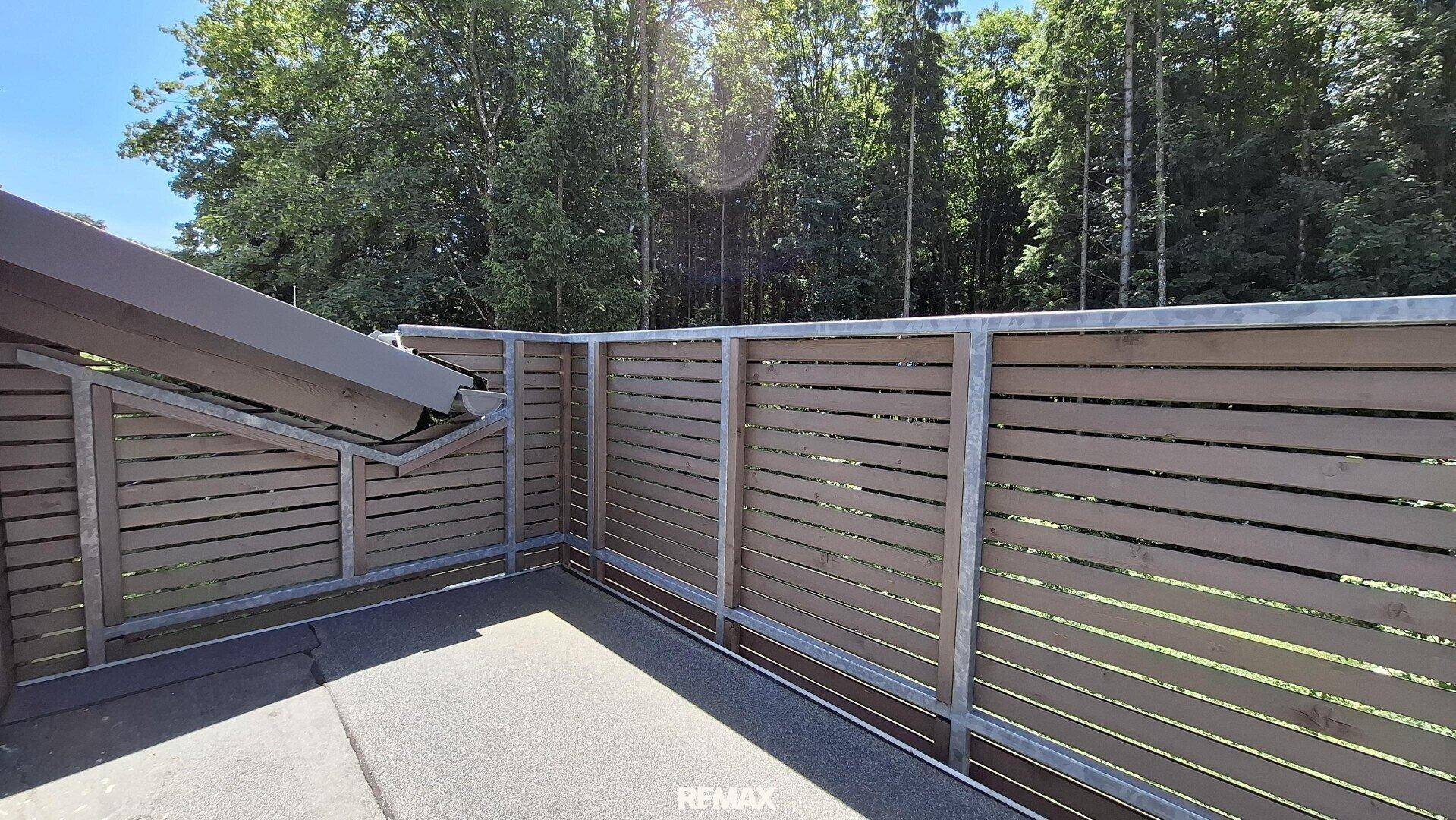 Privater Balkon mit Holzzaun und Blick auf die umliegenden Bäume und Natur.