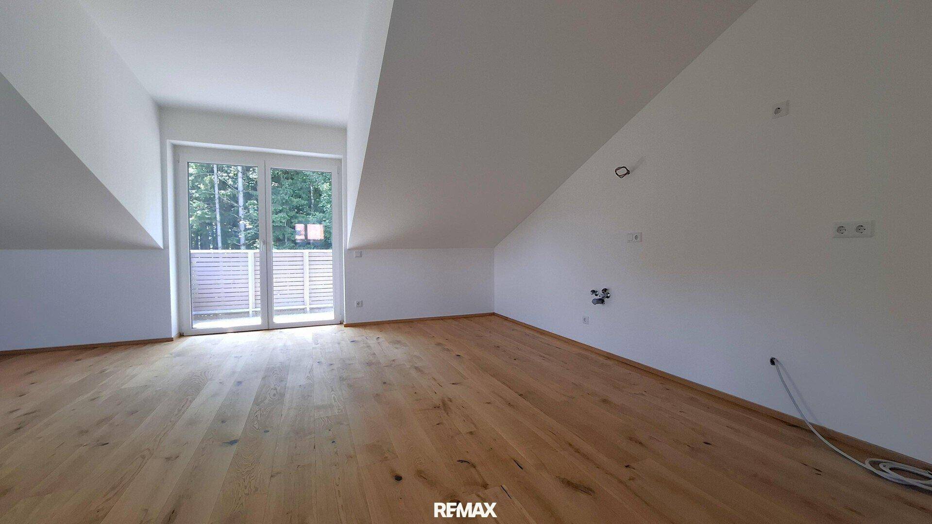 Lichtdurchfluteter Dachgeschossraum mit Holzboden und Zugang zu einem Außenbereich.