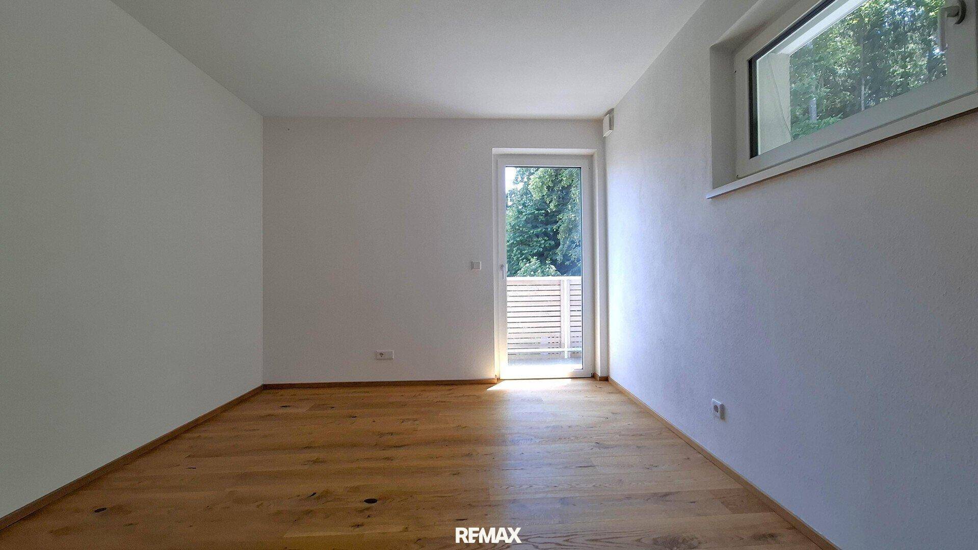 Geräumiges Schlafzimmer mit Holzboden und großer Glastür, die viel Tageslicht hereinlässt.