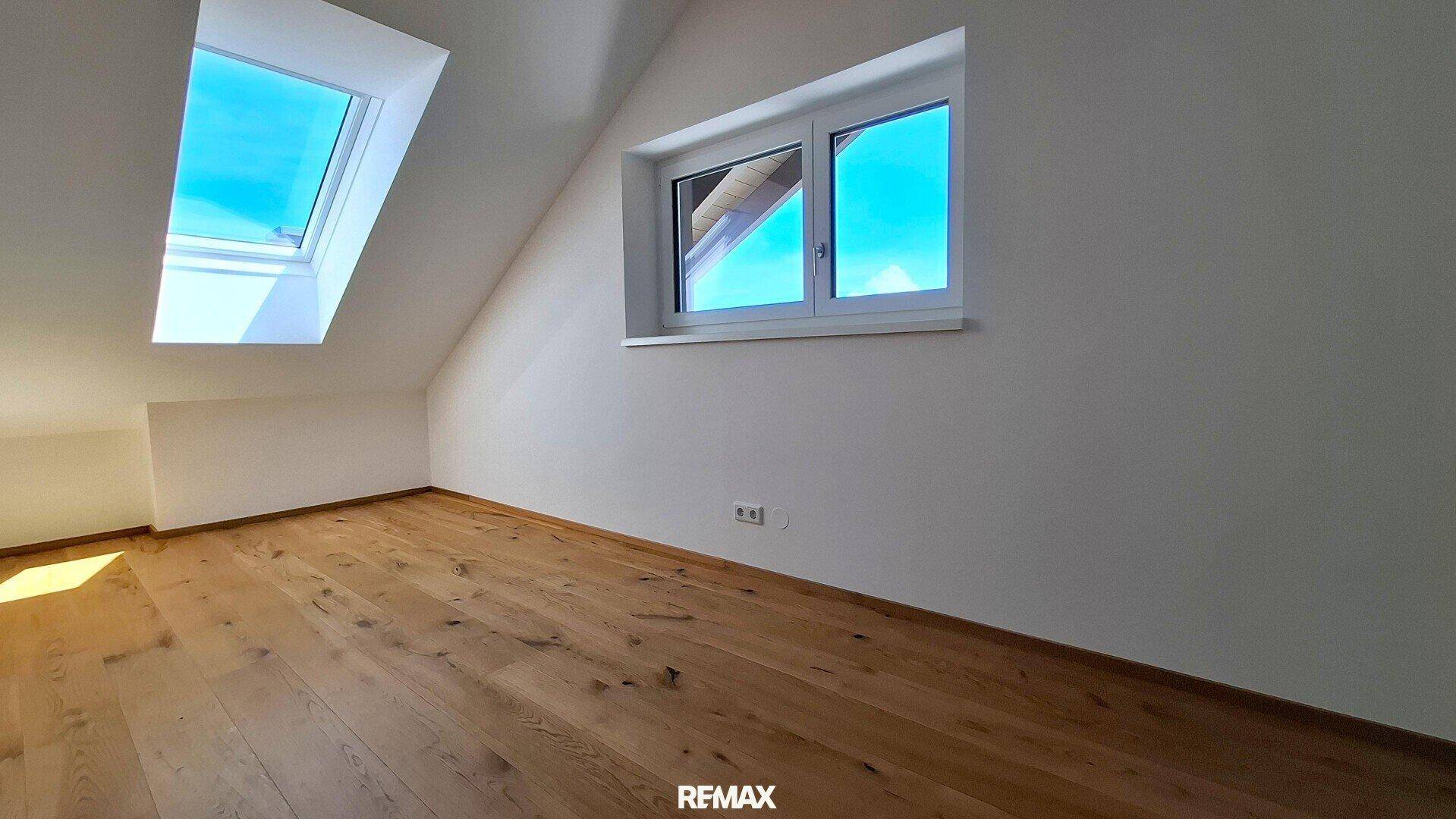 Helles Zimmer mit Holzboden, Fenster und zusätzlichem Dachfenster für viel Tageslicht.