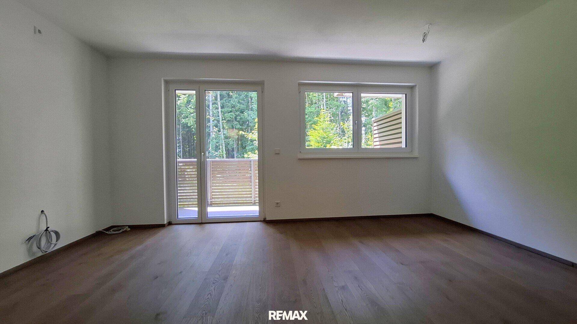 Geräumiger Wohnbereich mit dunklem Holzparkett, großen Fenstern und direktem Zugang zum Außenbereich.