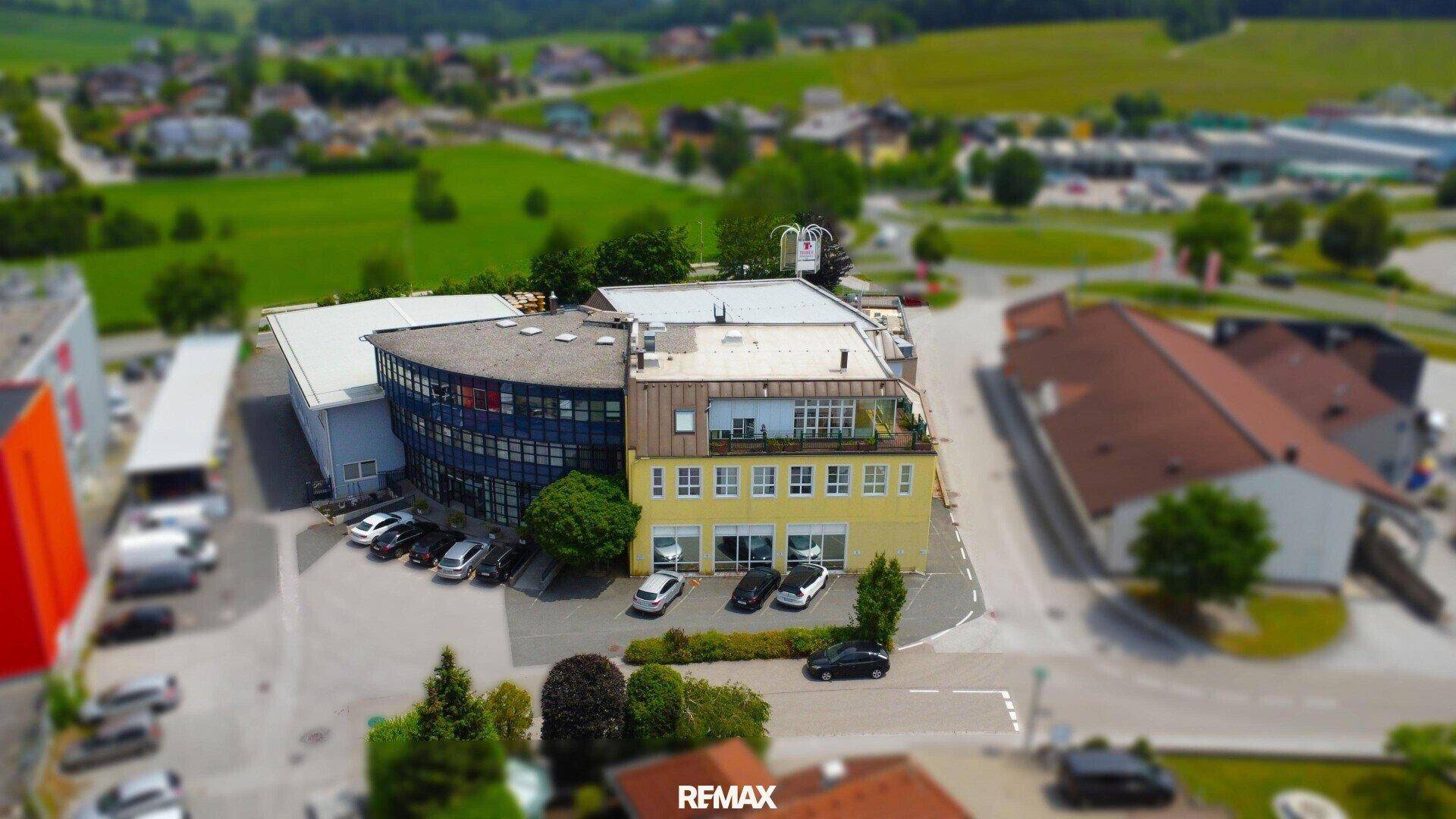 Luftaufnahme eines Geschäftskomplexes mit moderner Architektur, umgeben von Grünflächen und Parkplätzen.