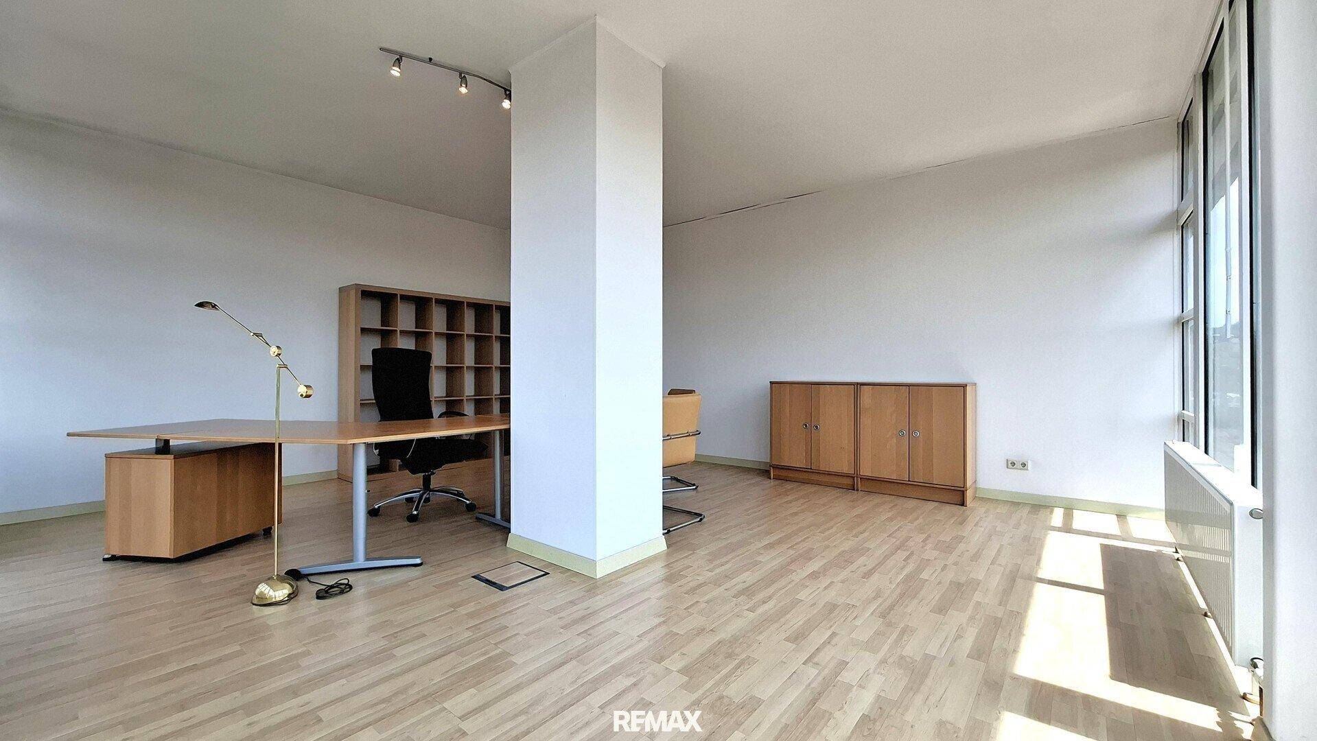 Großes, helles Büro mit Holzboden, einem Schreibtisch und einem Bücherregal an der Wand.