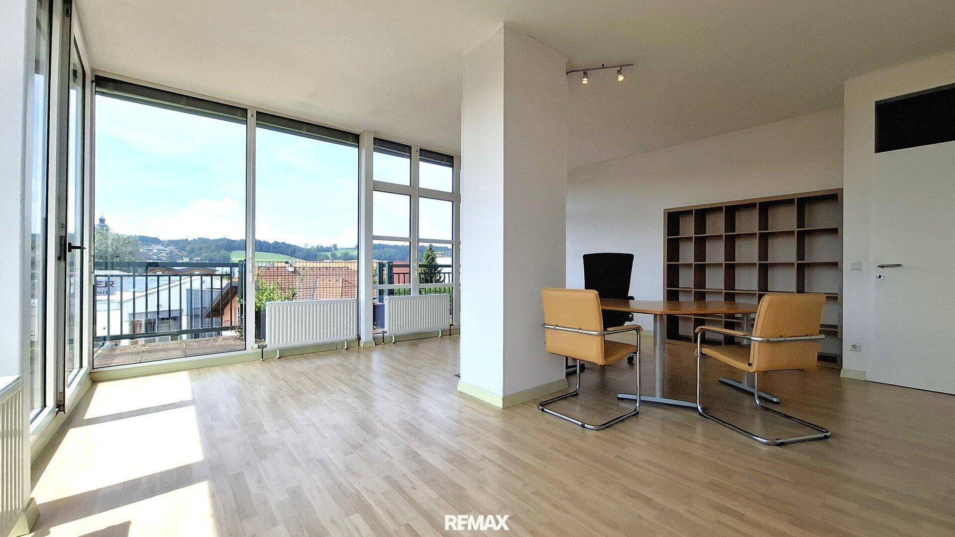Geräumiges Büro mit viel Tageslicht, Holzboden und einem Bücherregal im Hintergrund.