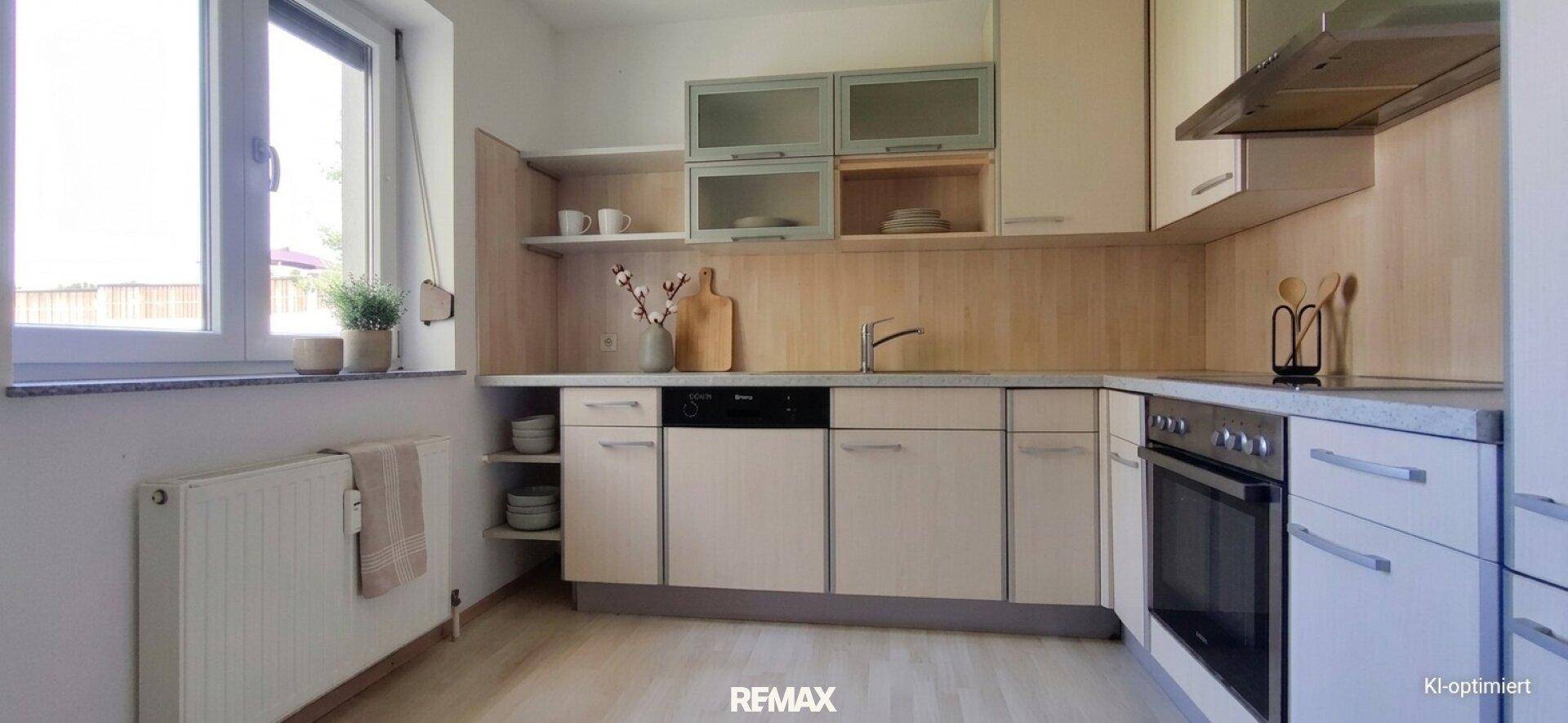 Helle Küche mit beigen Schränken, integrierten Geräten und Fensterblick nach draußen.