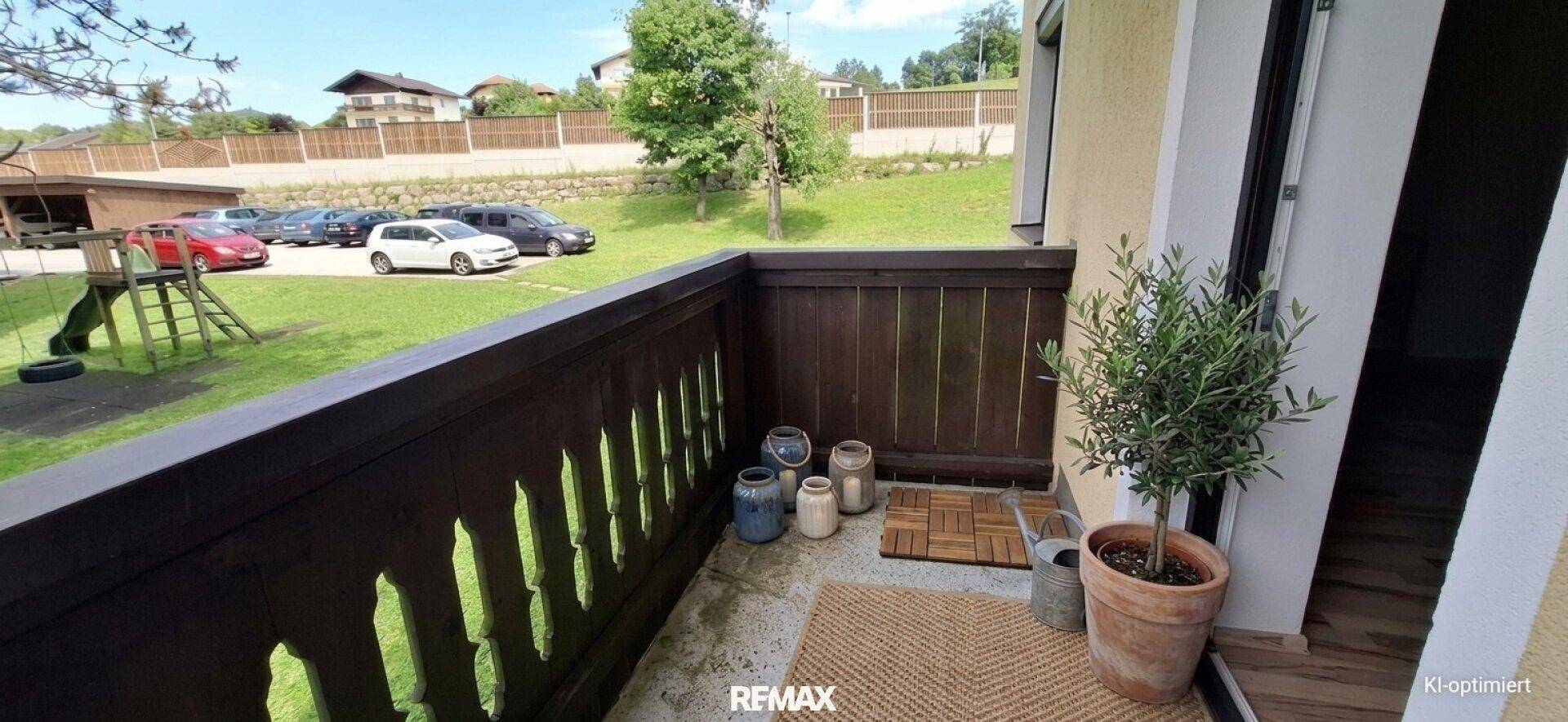 Kleiner Balkon mit Holzbalkon, Pflanzen und Blick auf den Garten und Parkplätze.
