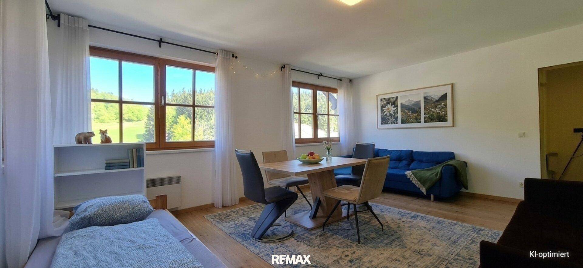 Heller Wohn- und Schlafbereich mit Holzboden, Esstisch, Sofa und weitem Blick ins Grüne durch große Fenster.