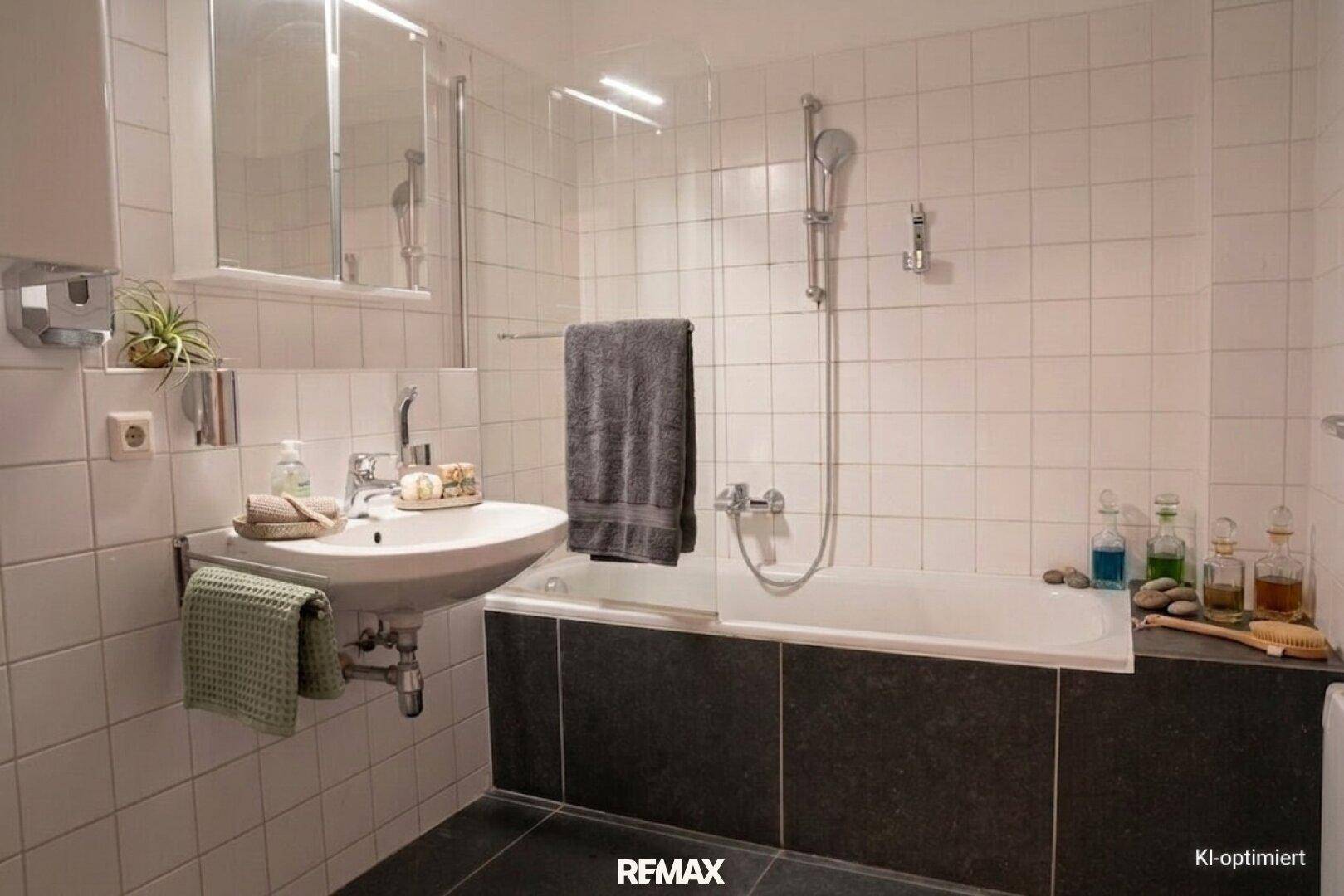 Helles Badezimmer mit Badewanne, Duschbereich, Waschbecken und weißen Fliesen an den Wänden und auf dem Boden.