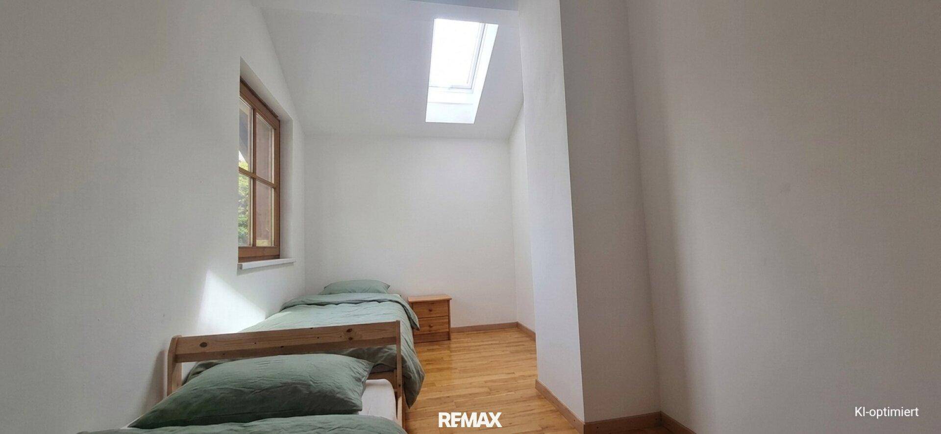 Einfaches Schlafzimmer mit zwei Einzelbetten, Holzboden, Fenster und einem Dachfenster für zusätzliche Helligkeit.