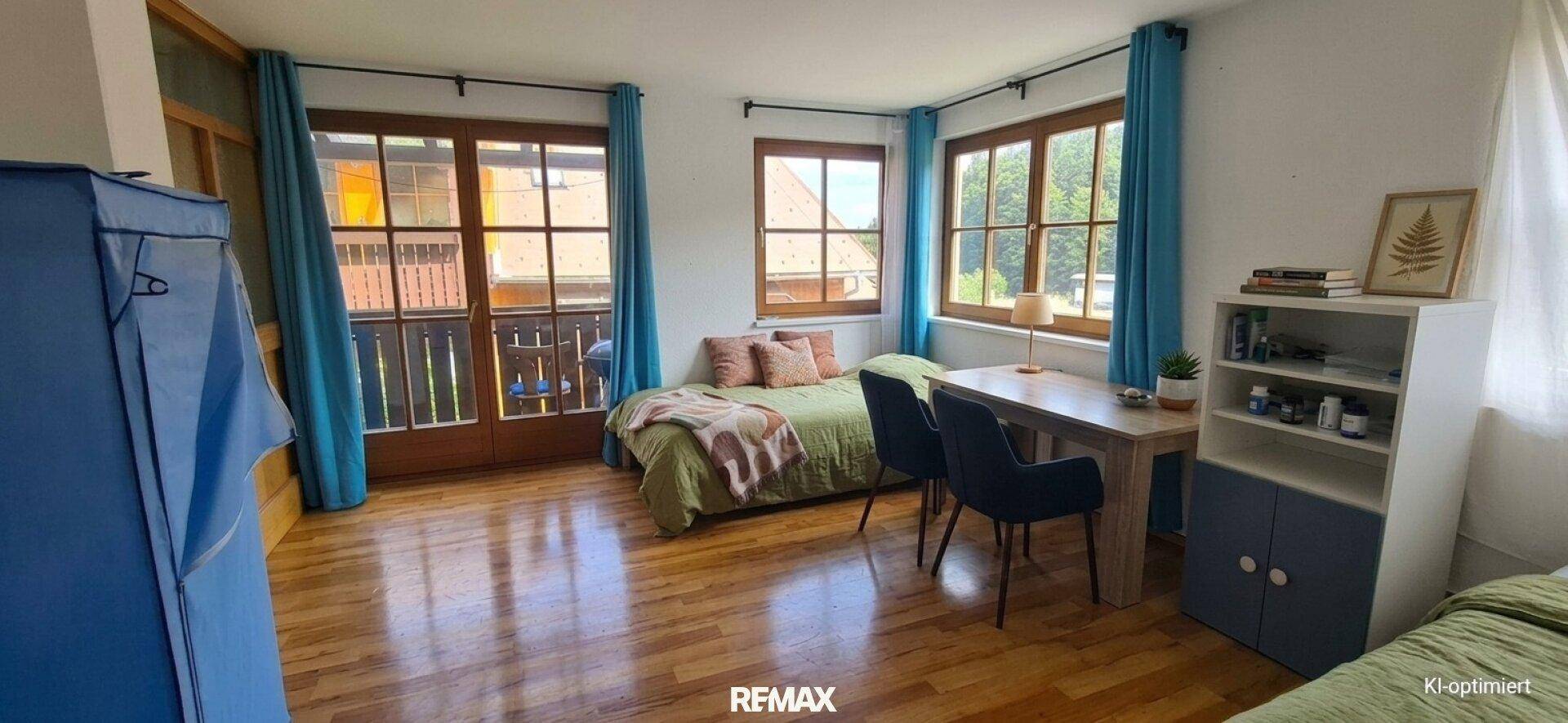 Geräumiger Wohn- und Schlafbereich mit Holzboden, Bett, Schreibtisch und direktem Zugang zu einem Balkon.