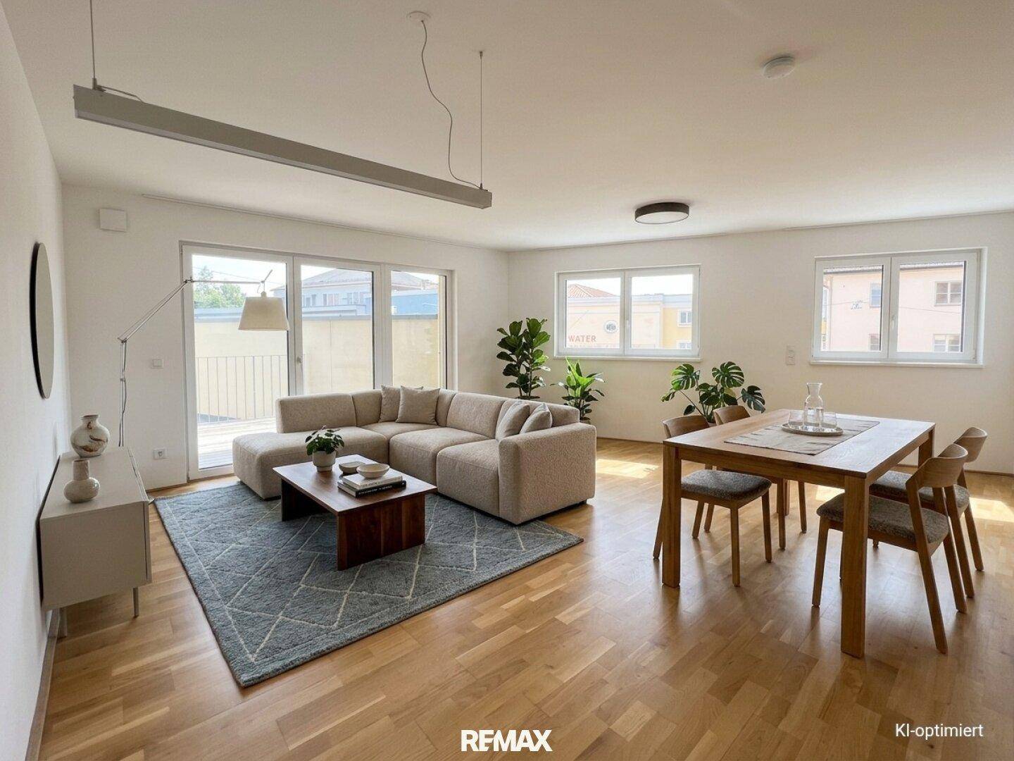 Heller offener Wohn- und Essbereich mit Parkettboden, beigem Sofa und Zugang zum Balkon.