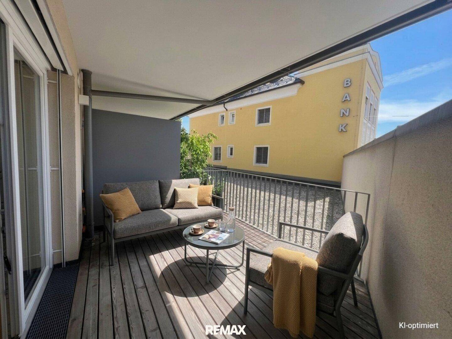 Sonniger Balkon mit Holzboden und bequemen Outdoor-Möbeln, ideal zum Entspannen im Freien.