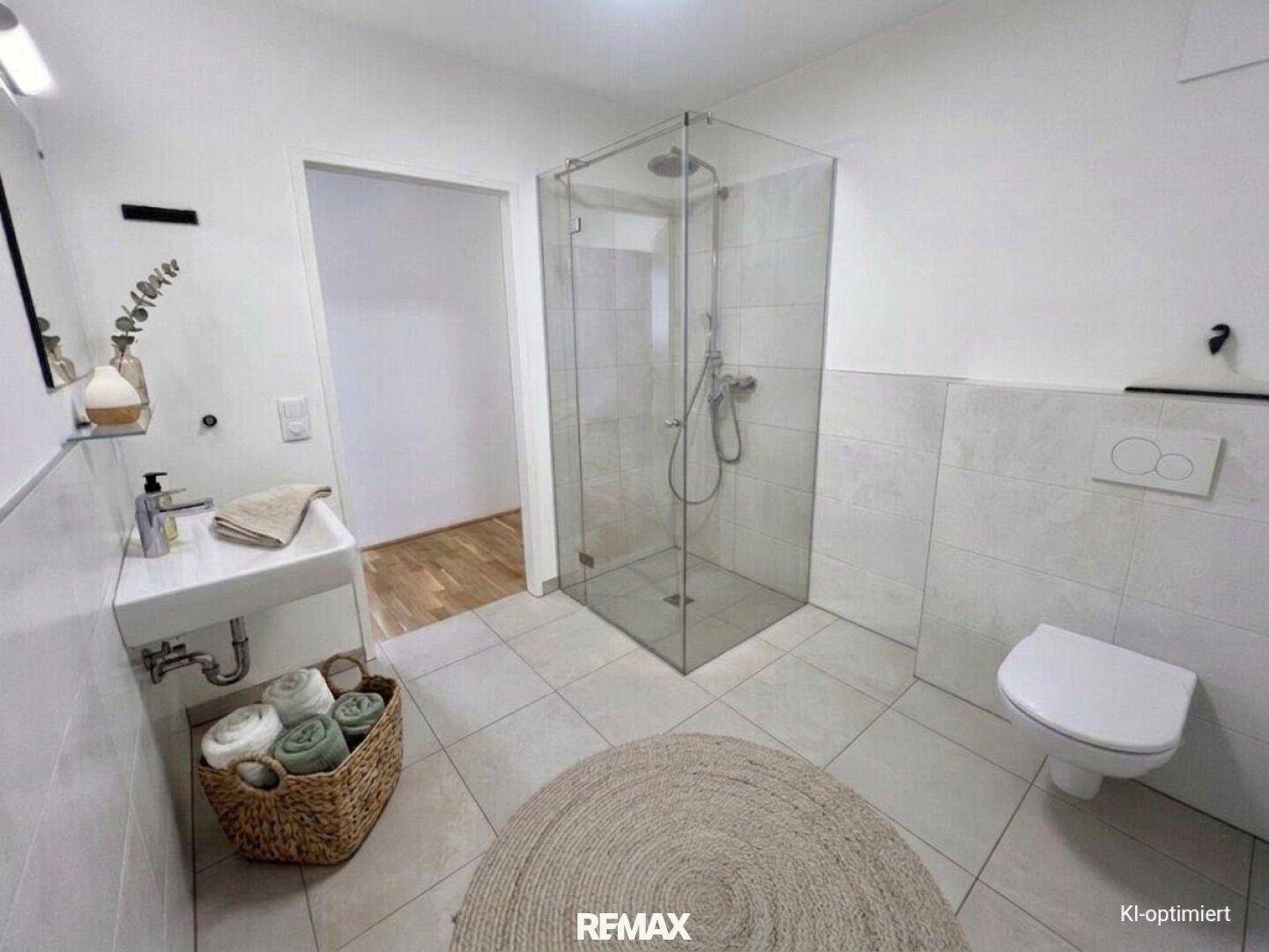Modernes Badezimmer mit ebenerdiger Glasdusche, Wand-WC und hellem Fliesenboden.