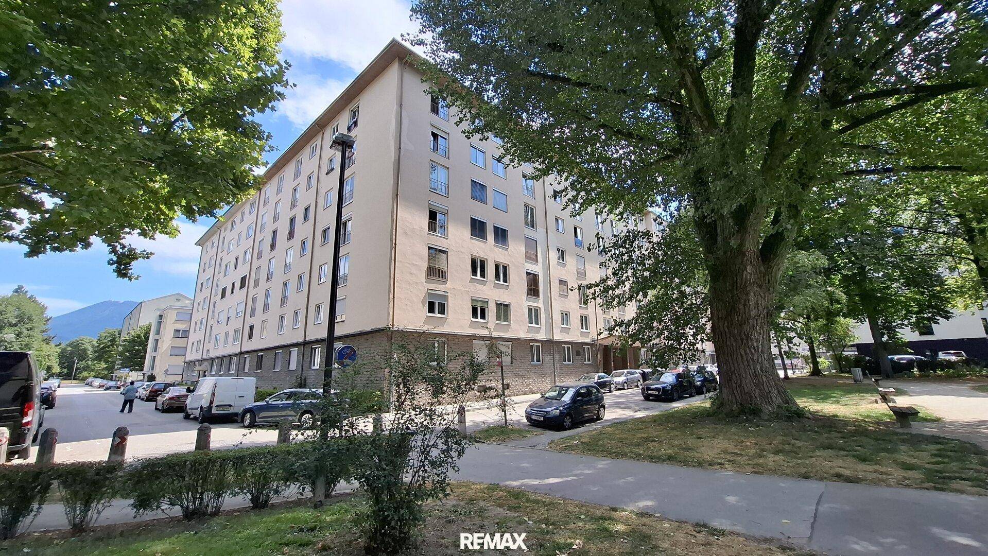 Mehrstöckiges Wohngebäude in einer grünen Umgebung mit Bäumen und Parkplätzen.