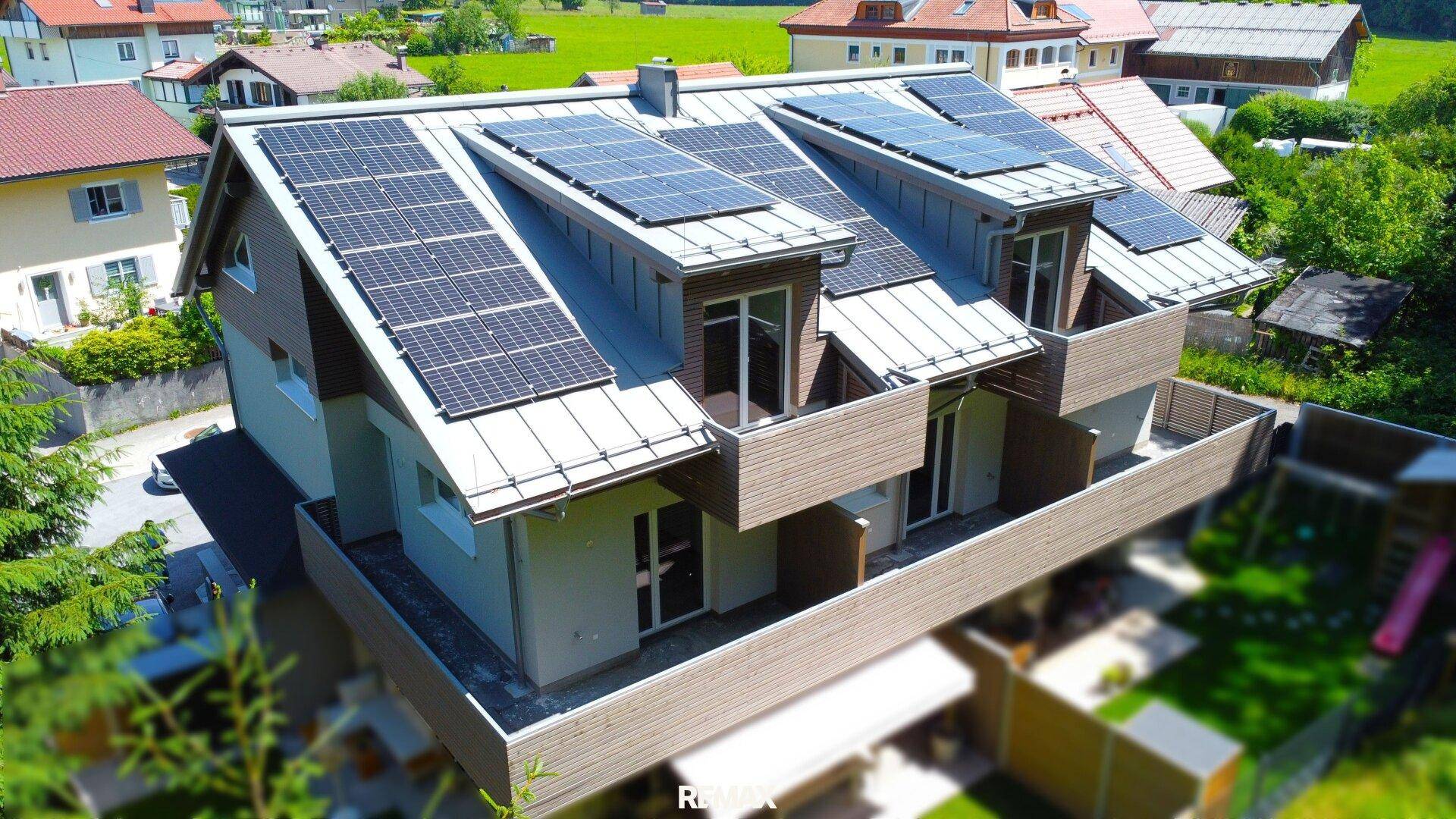 Wohnhaus mit moderner Architektur, Photovoltaikanlage und Balkonen, eingebettet in grüne Landschaft.