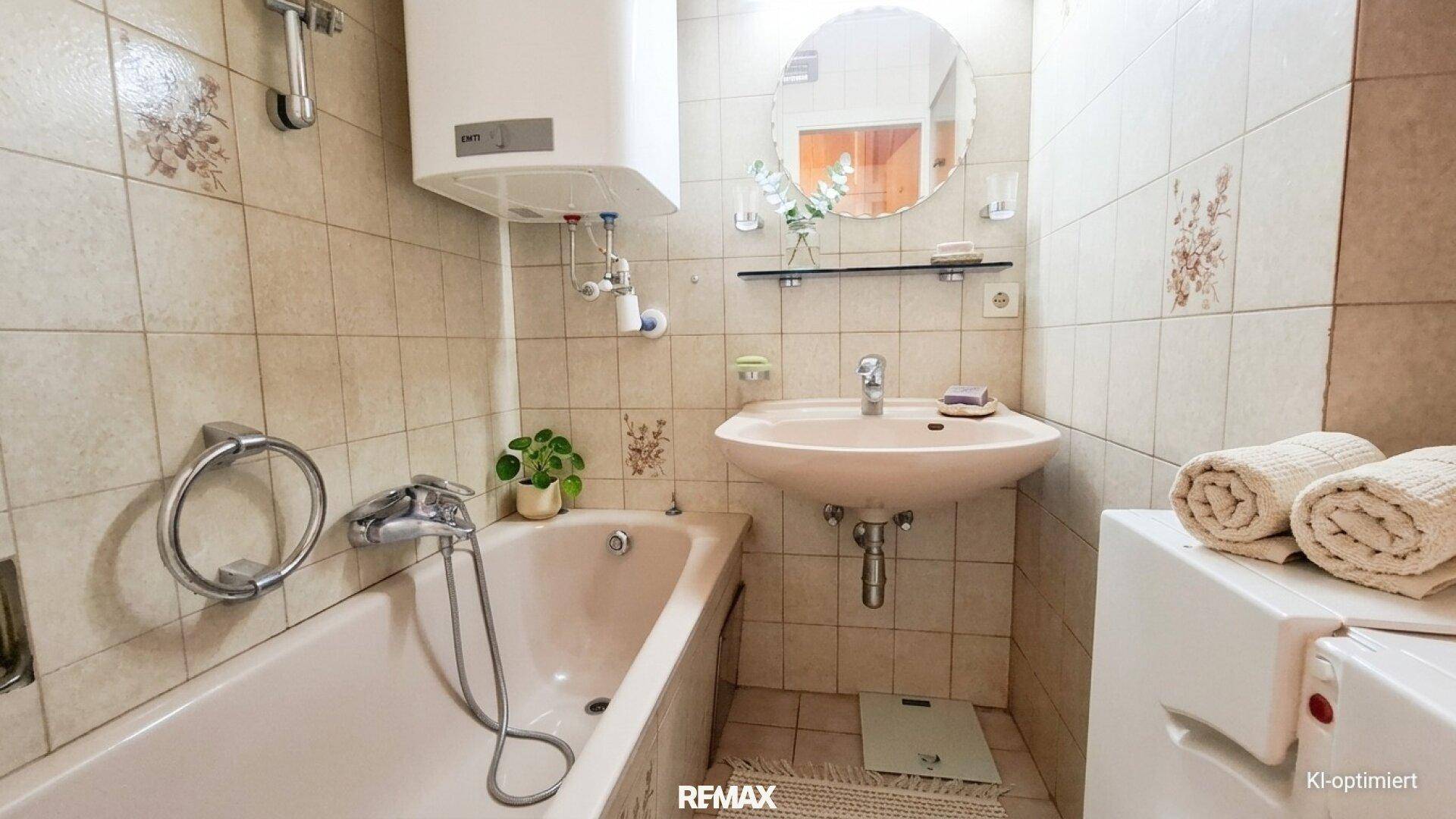 Kleines Badezimmer mit Badewanne, Waschbecken und Fliesen im 80er-Jahre-Stil.
