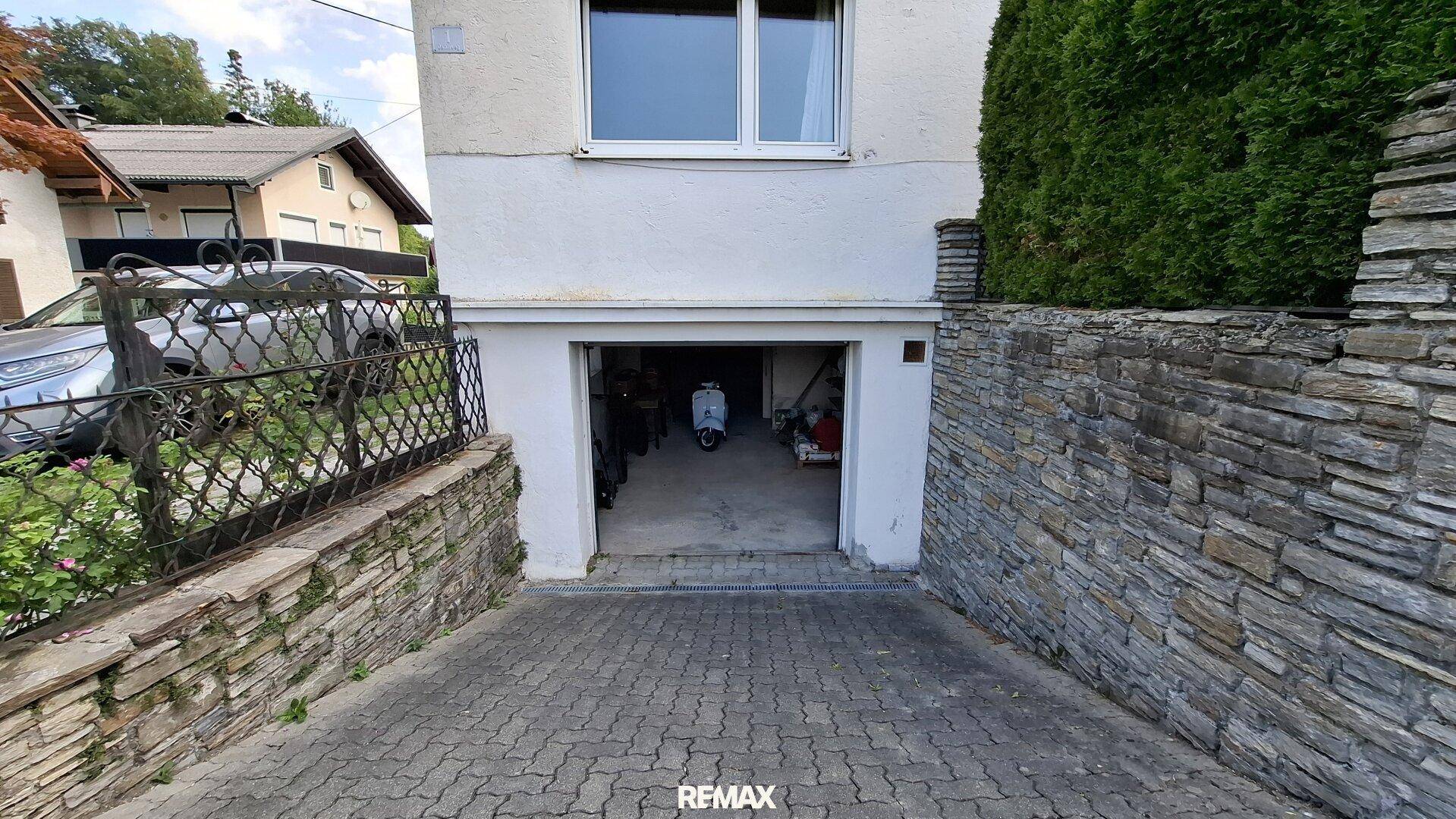 Einfahrt zur Garage unter dem Haus, umgeben von einer robusten Natursteinmauer.