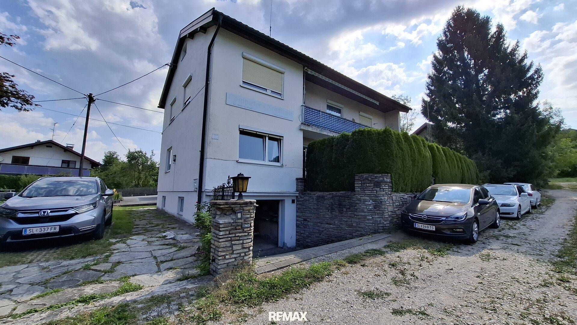 Vorderansicht des Hauses mit Einfahrt, geparkten Autos und Zugang zur Tiefgarage im Untergeschoss.