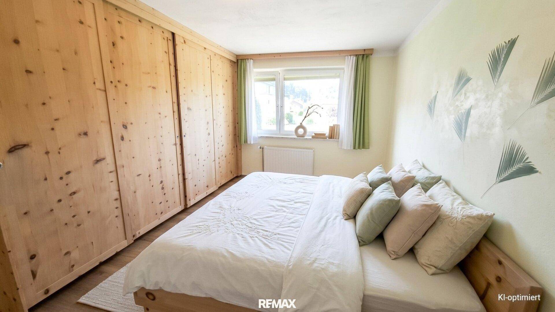 Schlafzimmer mit maßgefertigten Holzschränken und einem großen Fenster mit Blick ins Grüne.