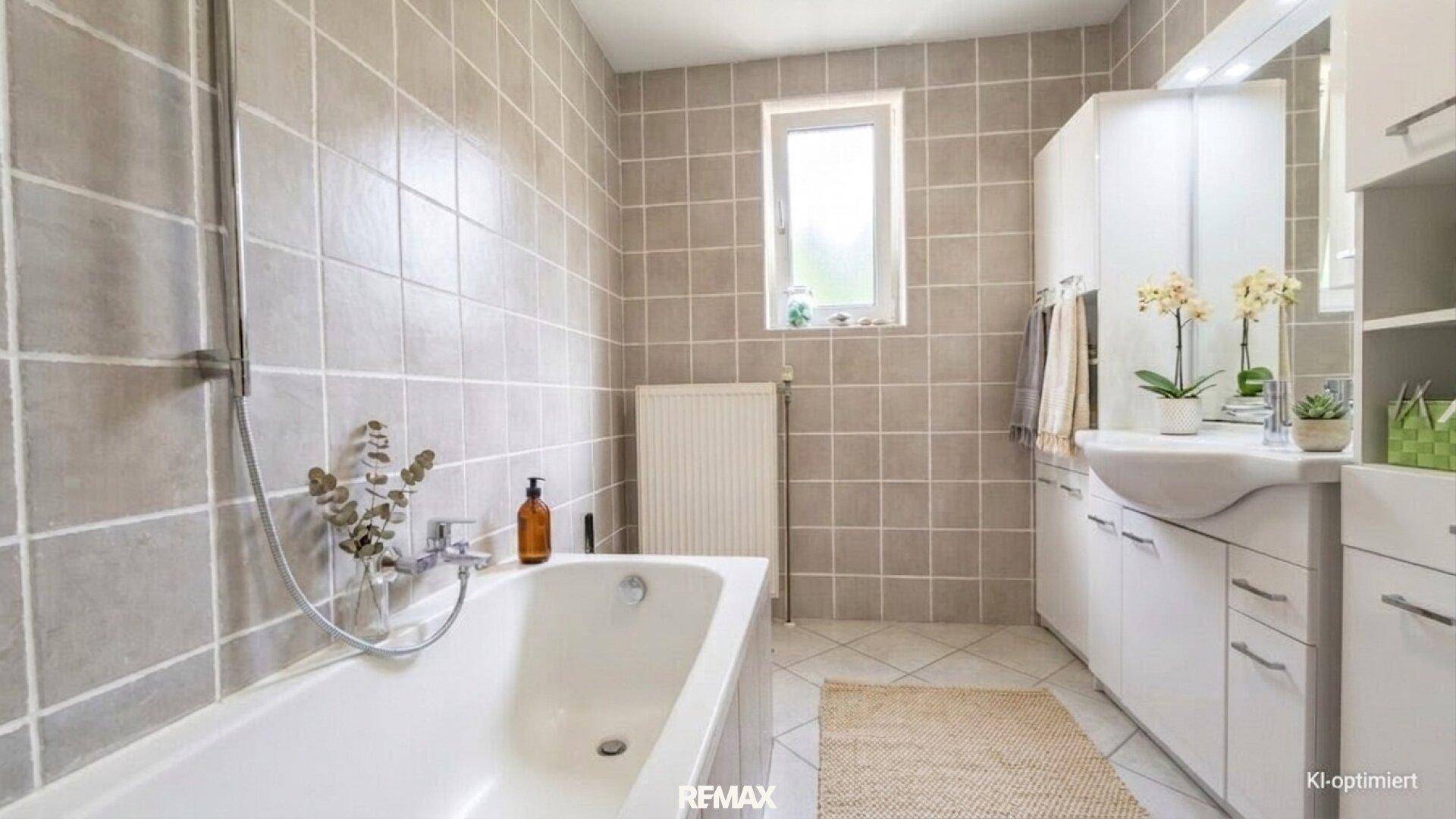Badezimmer mit beigefarbenen Fliesen, Badewanne, Waschbecken und einem Fenster für Tageslicht.