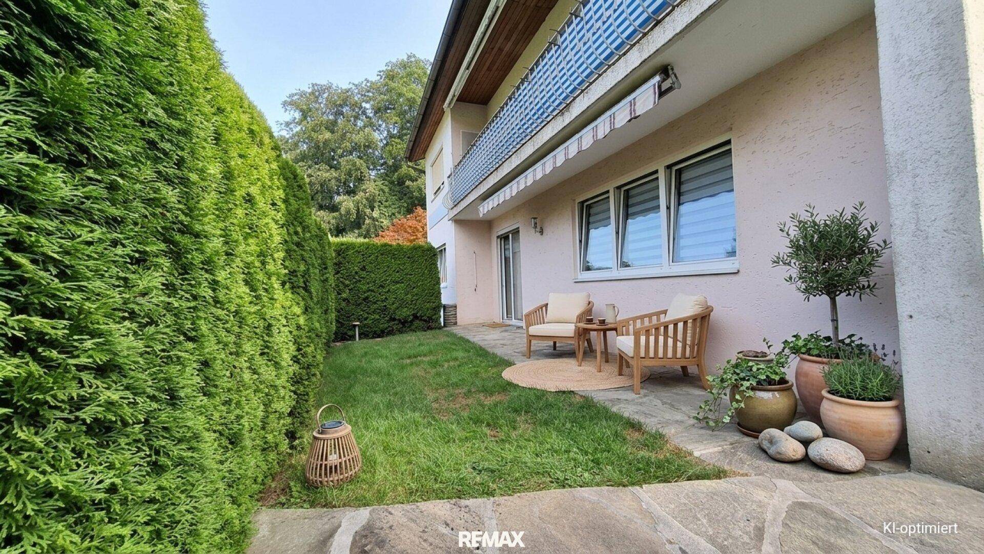 Gemütlicher Gartenbereich mit Sitzgelegenheiten und hoher Hecke neben dem Haus auf einer Steinterrasse.