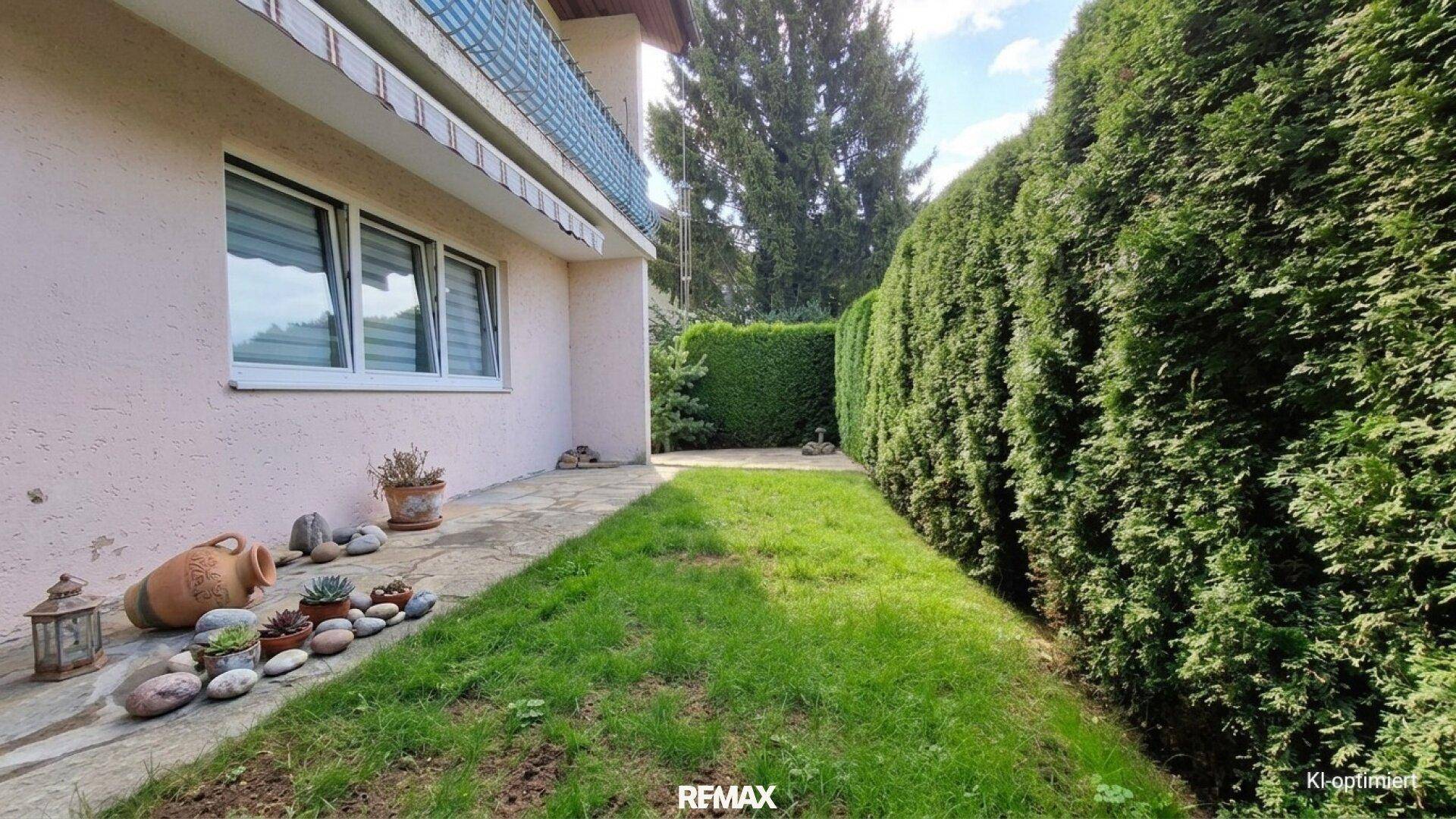 Seitlicher Gartenbereich mit Rasenfläche und hoher Hecke, die zum Haus führt und Privatsphäre bietet.