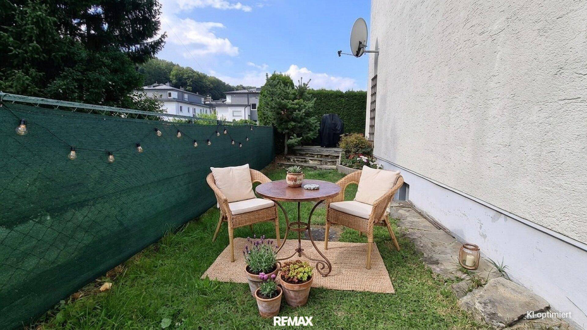 Kleiner Sitzbereich im Garten mit Korbmöbeln und grüner Umzäunung, ideal zum Entspannen.