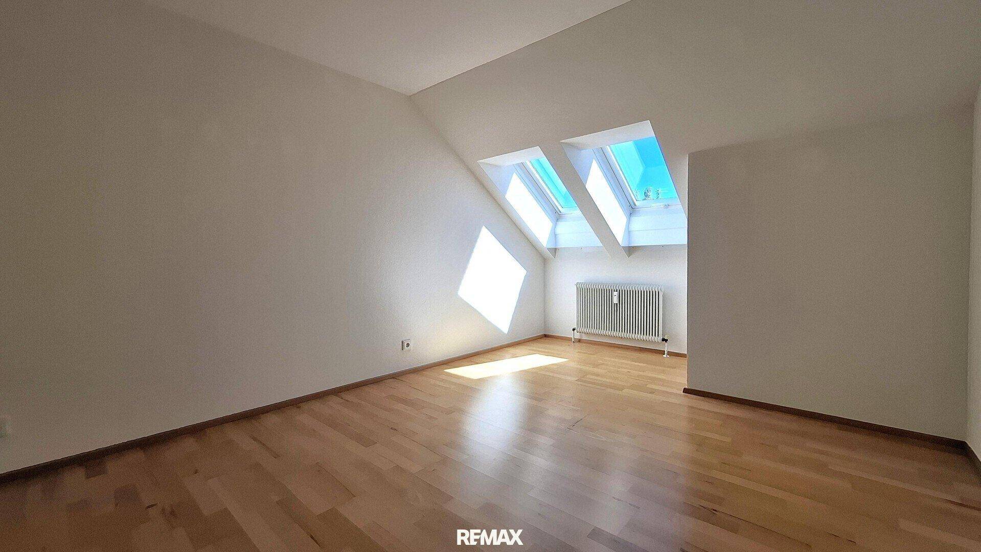 Heller, leerer Raum mit Parkettboden und Dachfenstern, die viel Sonnenlicht hereinlassen.