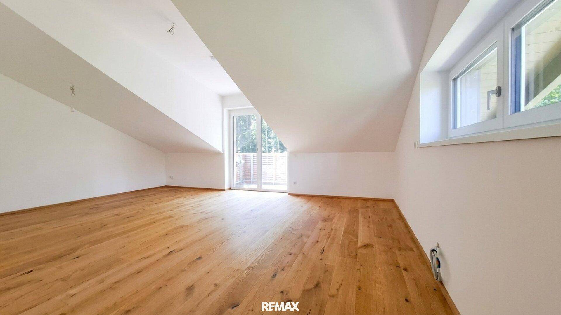 Geräumiger, leerer Raum mit Holzboden, Dachschrägen und Zugang zu einem Balkon.