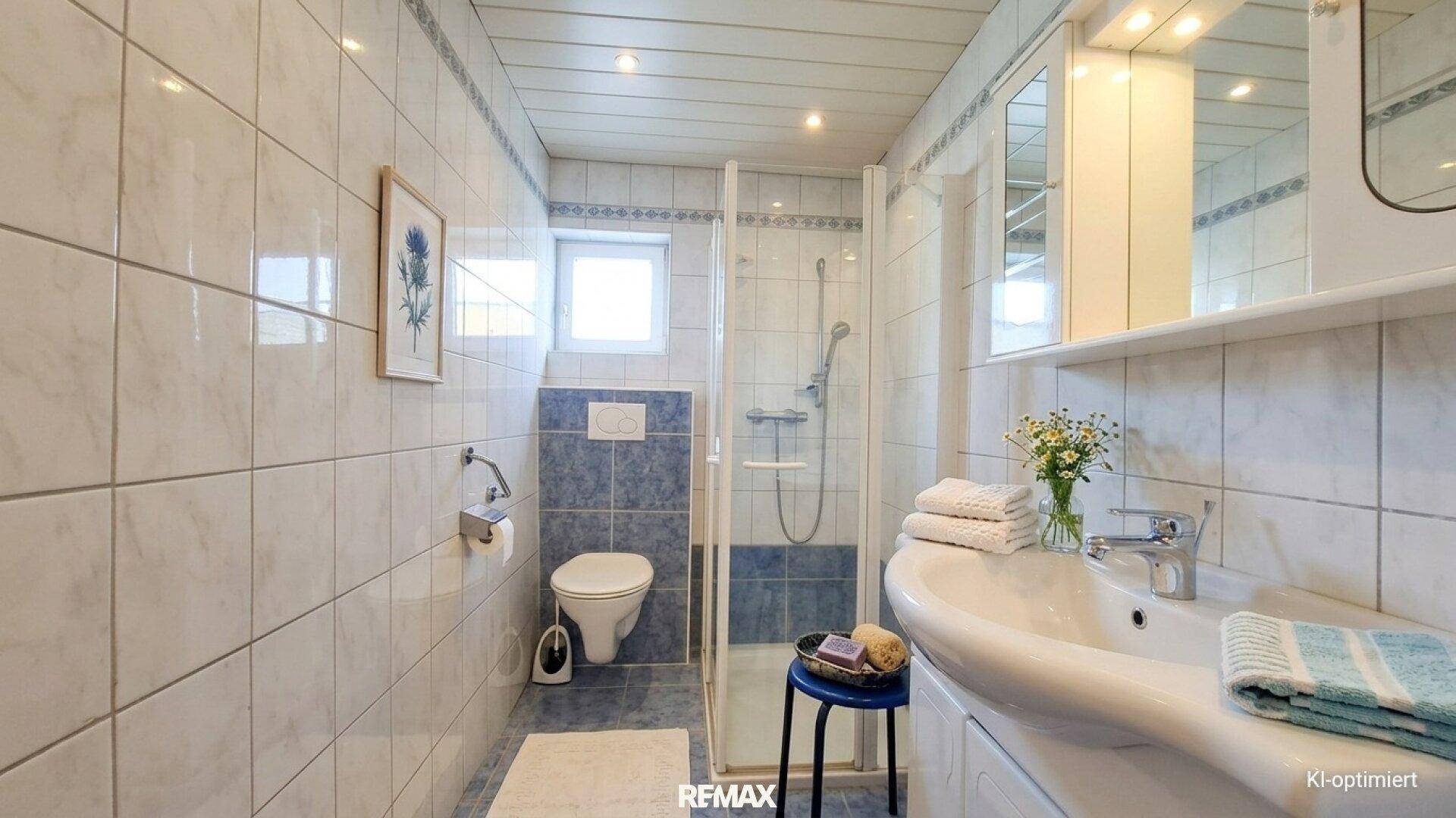 Badezimmer mit Dusche, WC, Waschbecken und hellblauen Fliesen.