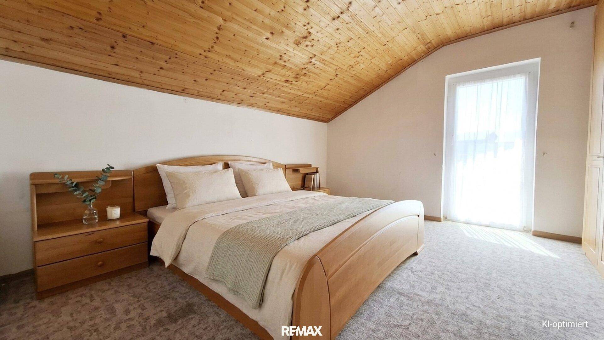 Schlafzimmer im Dachgeschoss mit Holzdachschräge und Zugang zum Balkon.